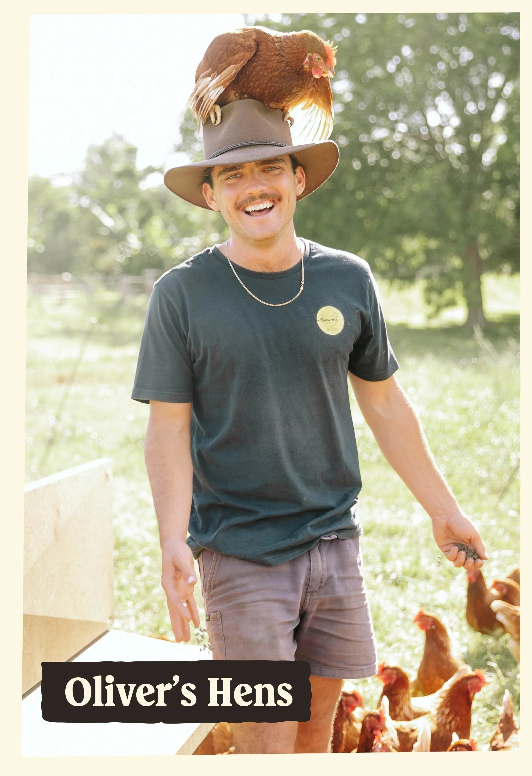 A smiling man wearing a wide-brimmed hat with a chicken perched on top, standing outdoors with chickens in the background, labeled 'Oliver's Hens'.
