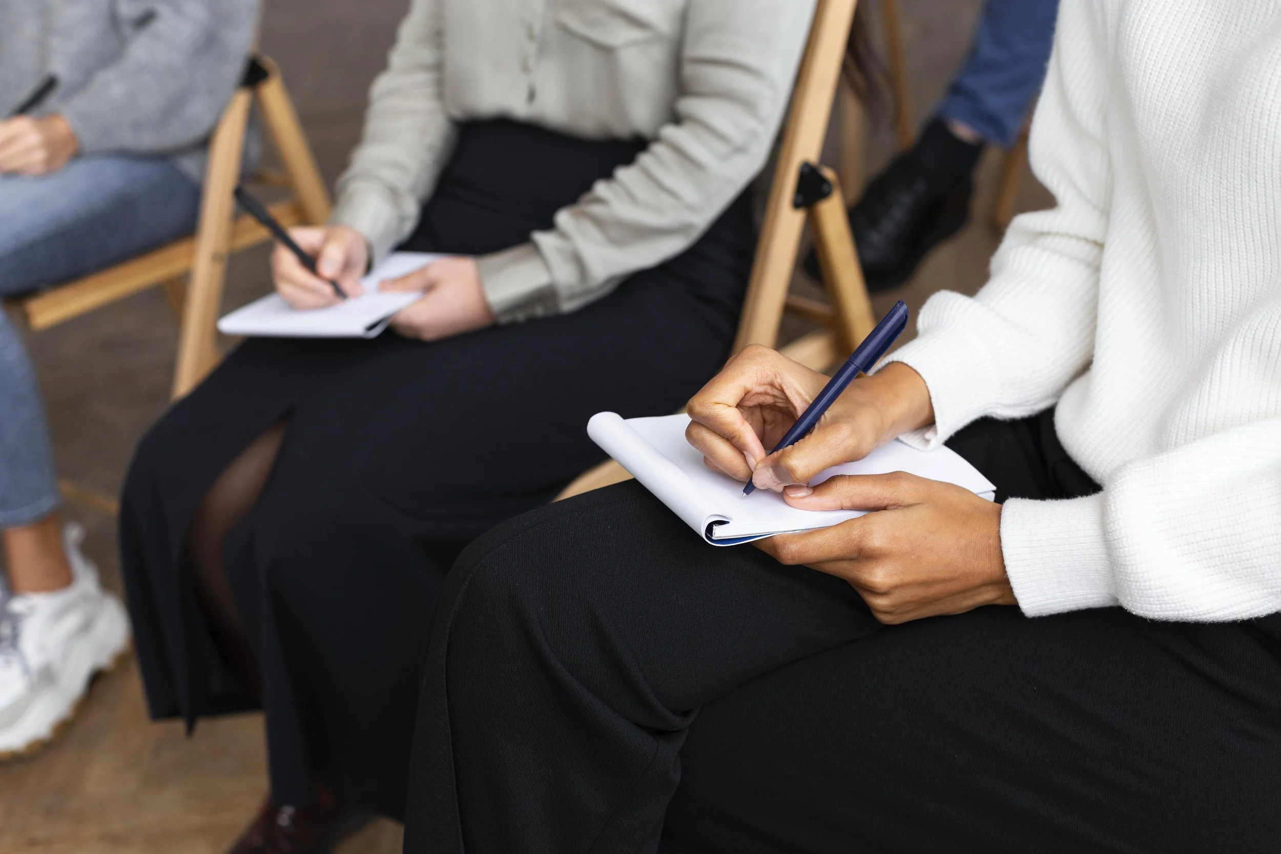 People sitting in a meeting, taking notes on notepads.