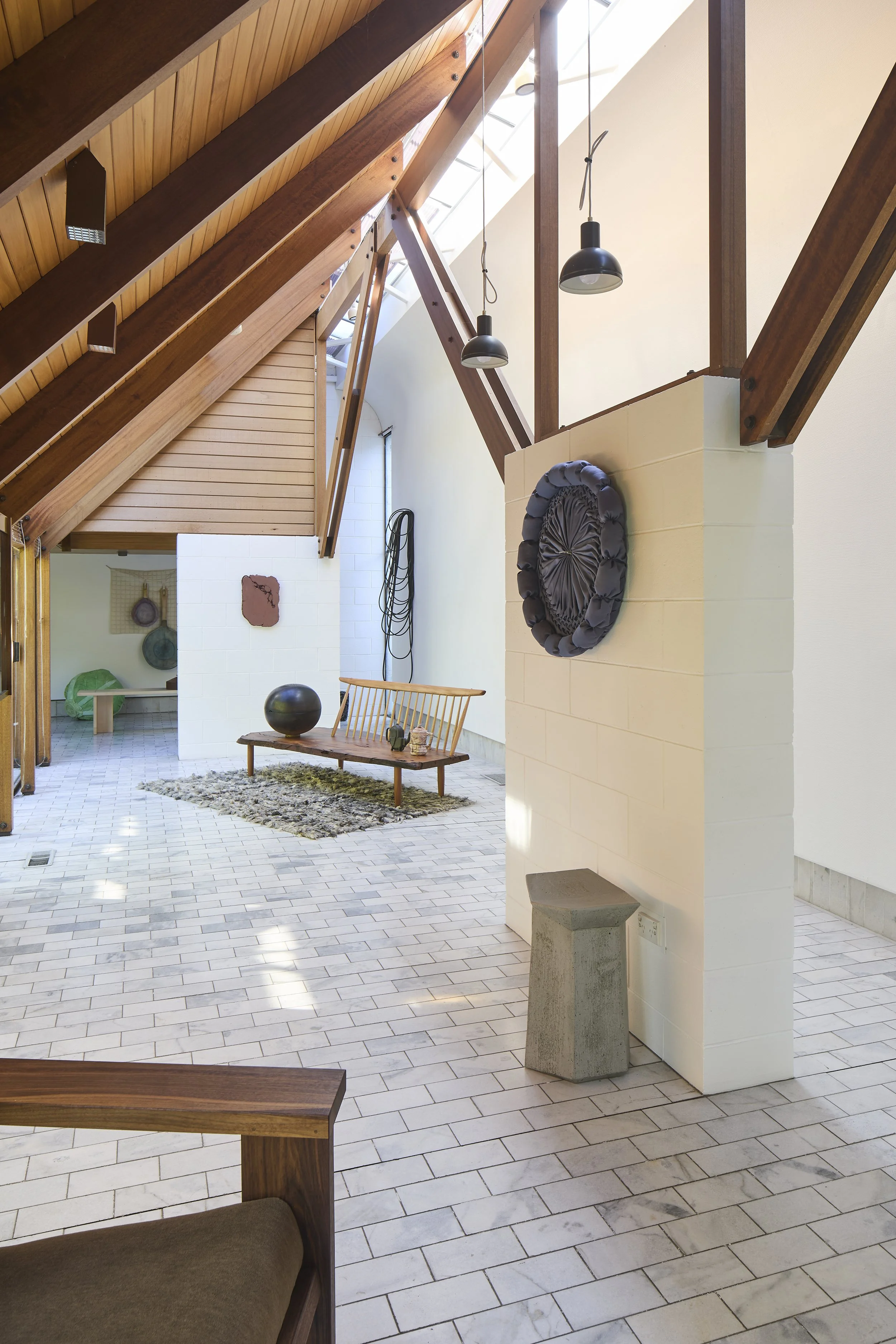 Interior view of a modern home with wooden beams and vaulted ceiling, pendant lighting, white walls, tiled flooring, a wooden bench with decor, and abstract art on the walls.