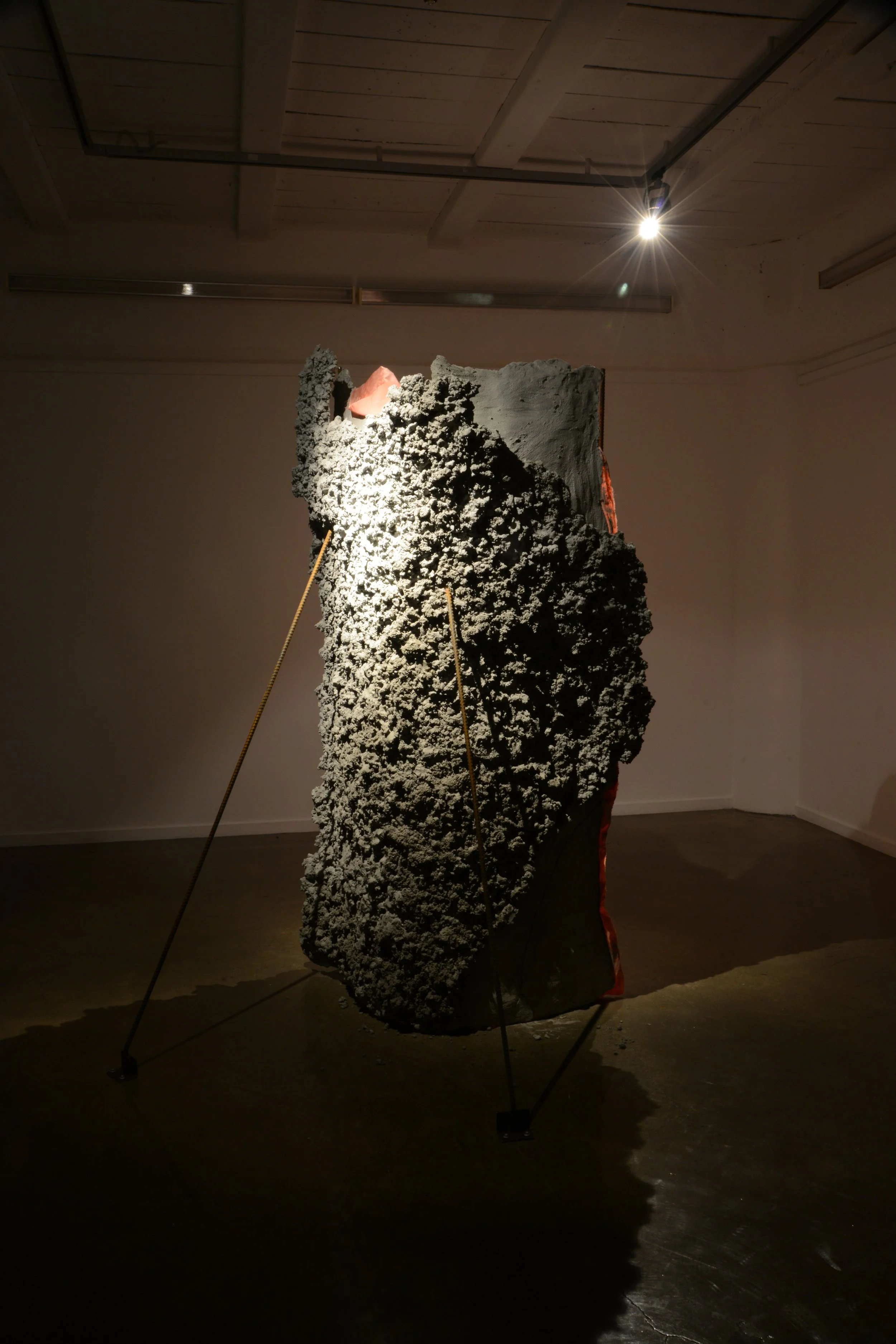 Abstract textured sculpture on a support stand in an art gallery, illuminated by a spotlight.