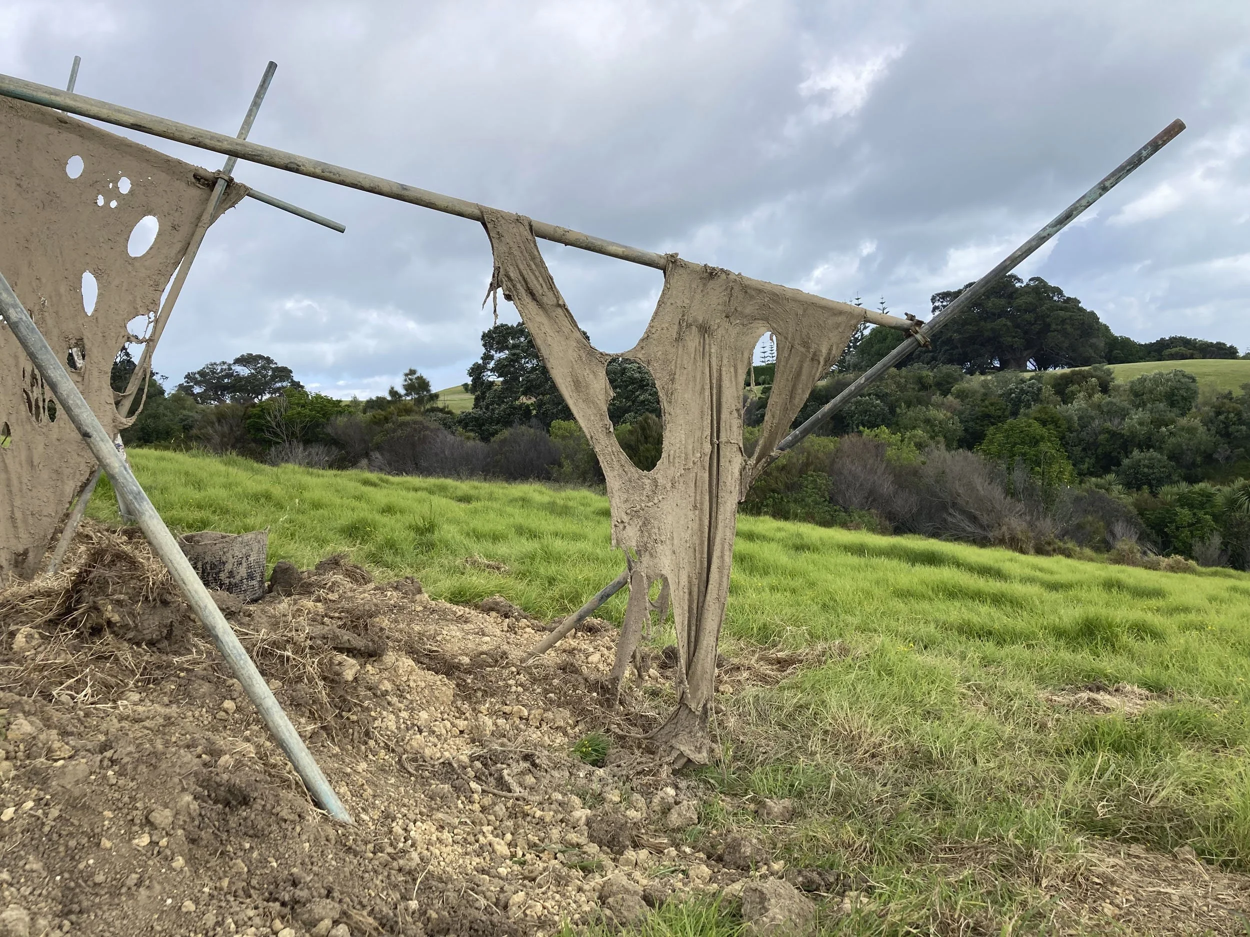 Dried fabric hanging on a clothesline in a grassy outdoor area with rolling hills and trees in the background.