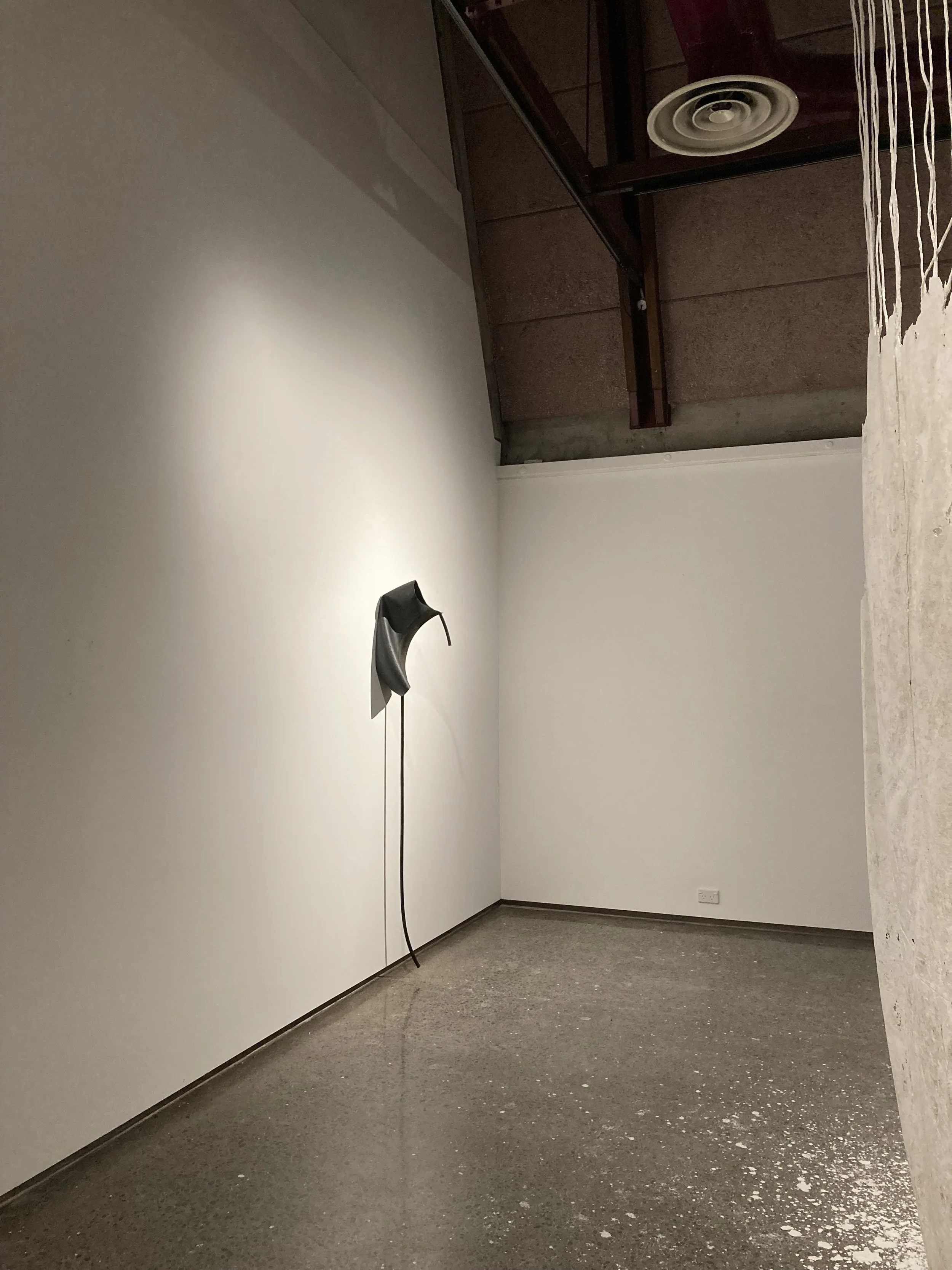 Minimalist art gallery with a sculpture resembling a phone handset mounted on a white wall.