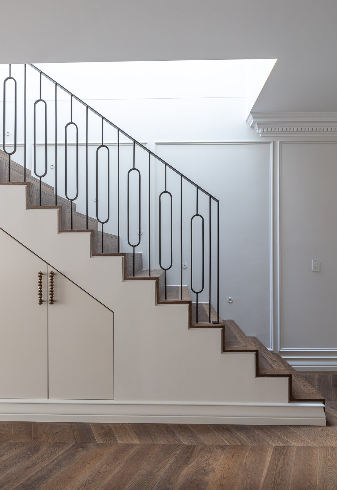 Interior staircase with dark metal railing, white walls, wooden stairs, and an overhead skylight.