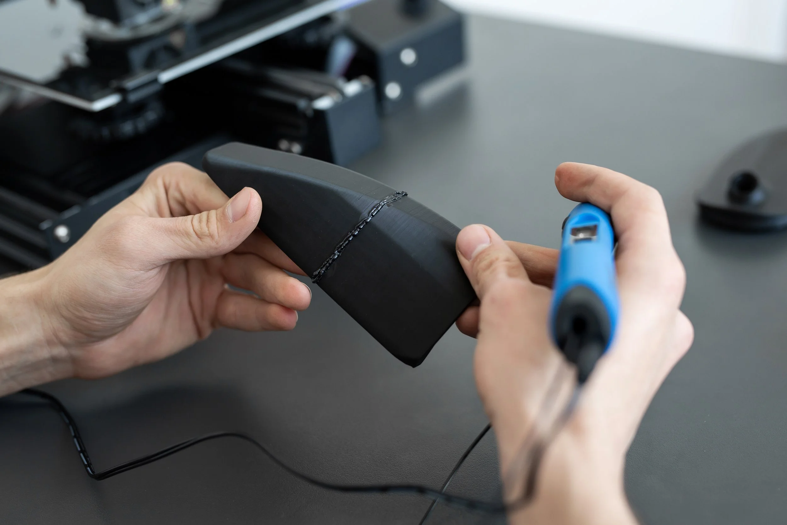A hand holds a 3D printing project with resin on it against a blurred background.