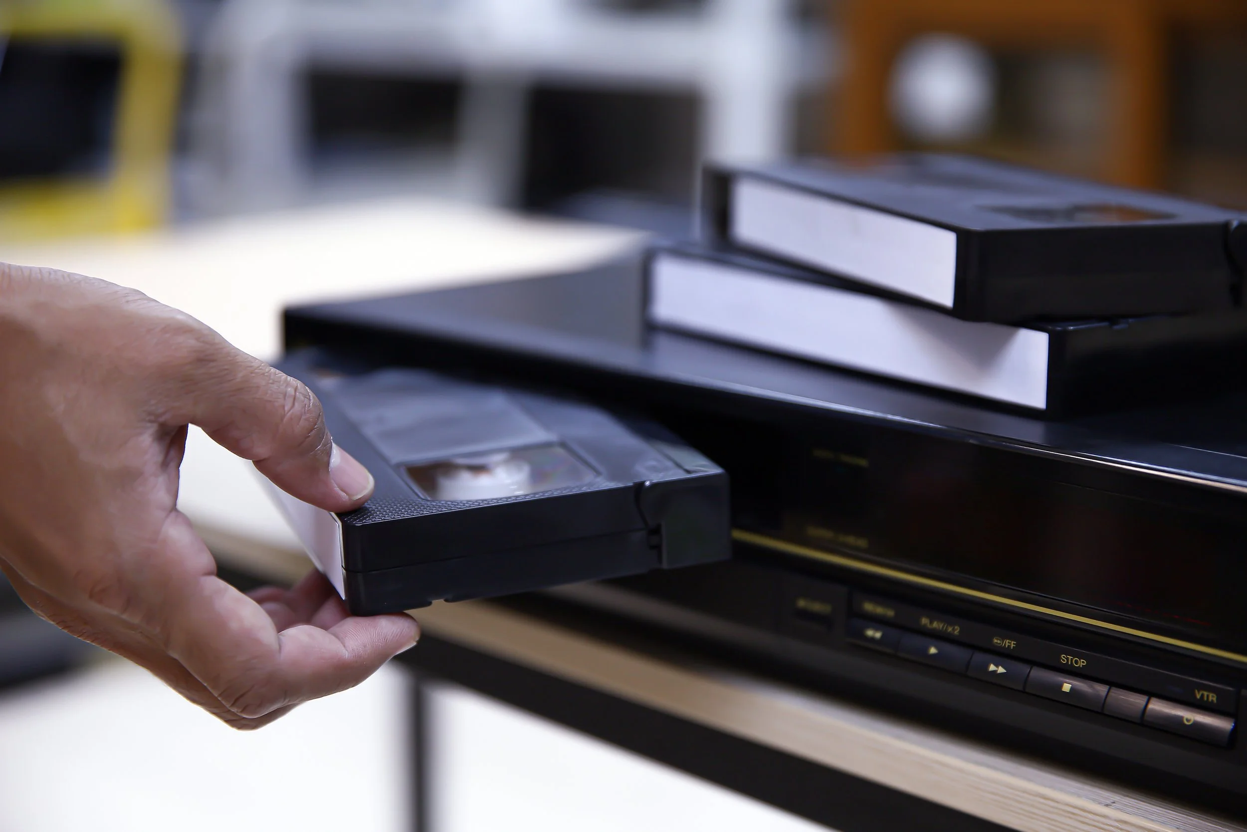 A hand holds a VCR tape as it is being taken out of a VCR player with a blurred background.