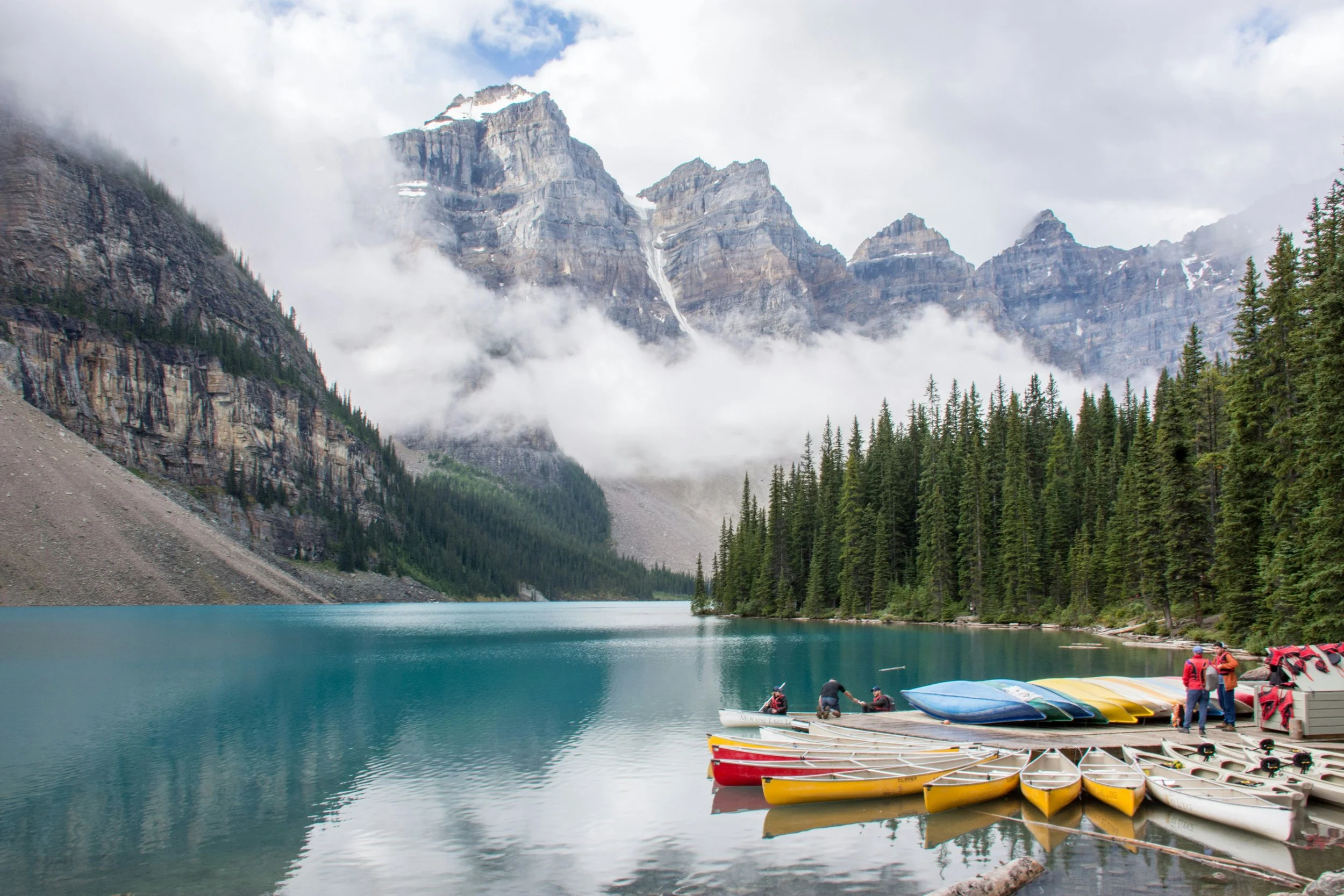 Colorful kayaks lined up on turquoise lake beneath snowy mountains and pine trees, symbolizing guidance, calm and navigating caregiver waters