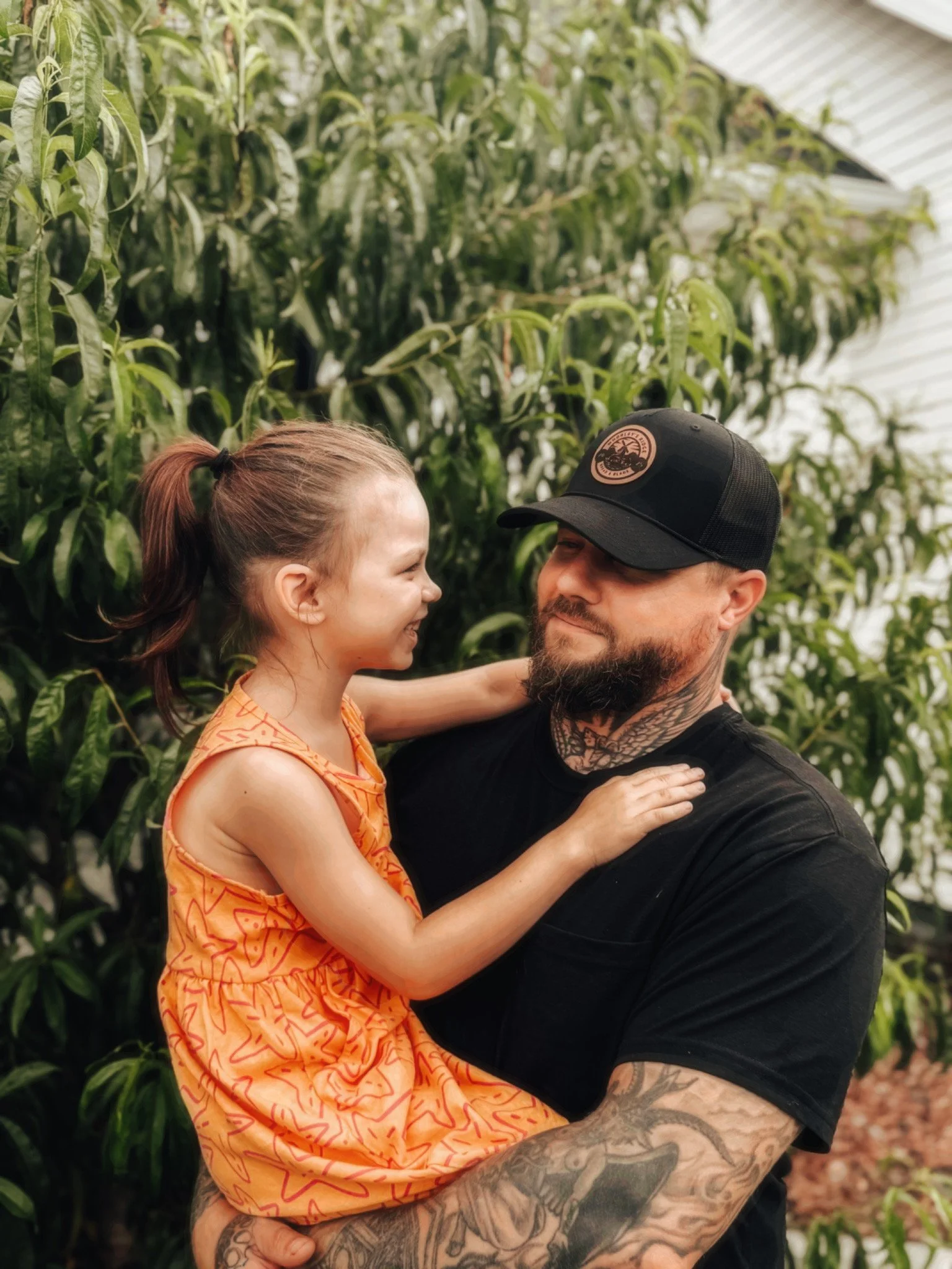 A man holding a smiling young girl in a green leafy outdoor setting.