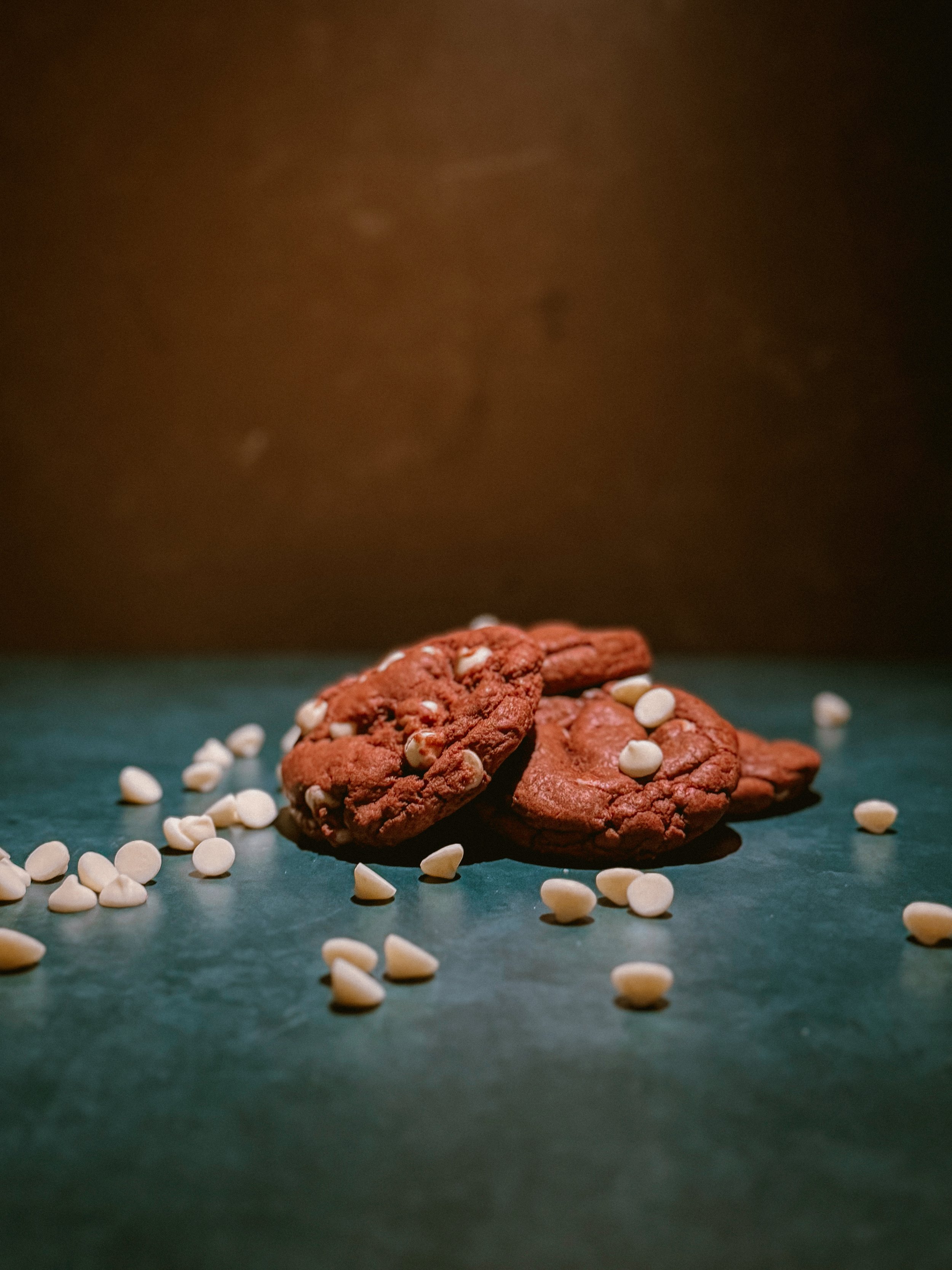 Chocolate chip cookies sprinkled with white white chocolate chips on a dark surface with a dark background.