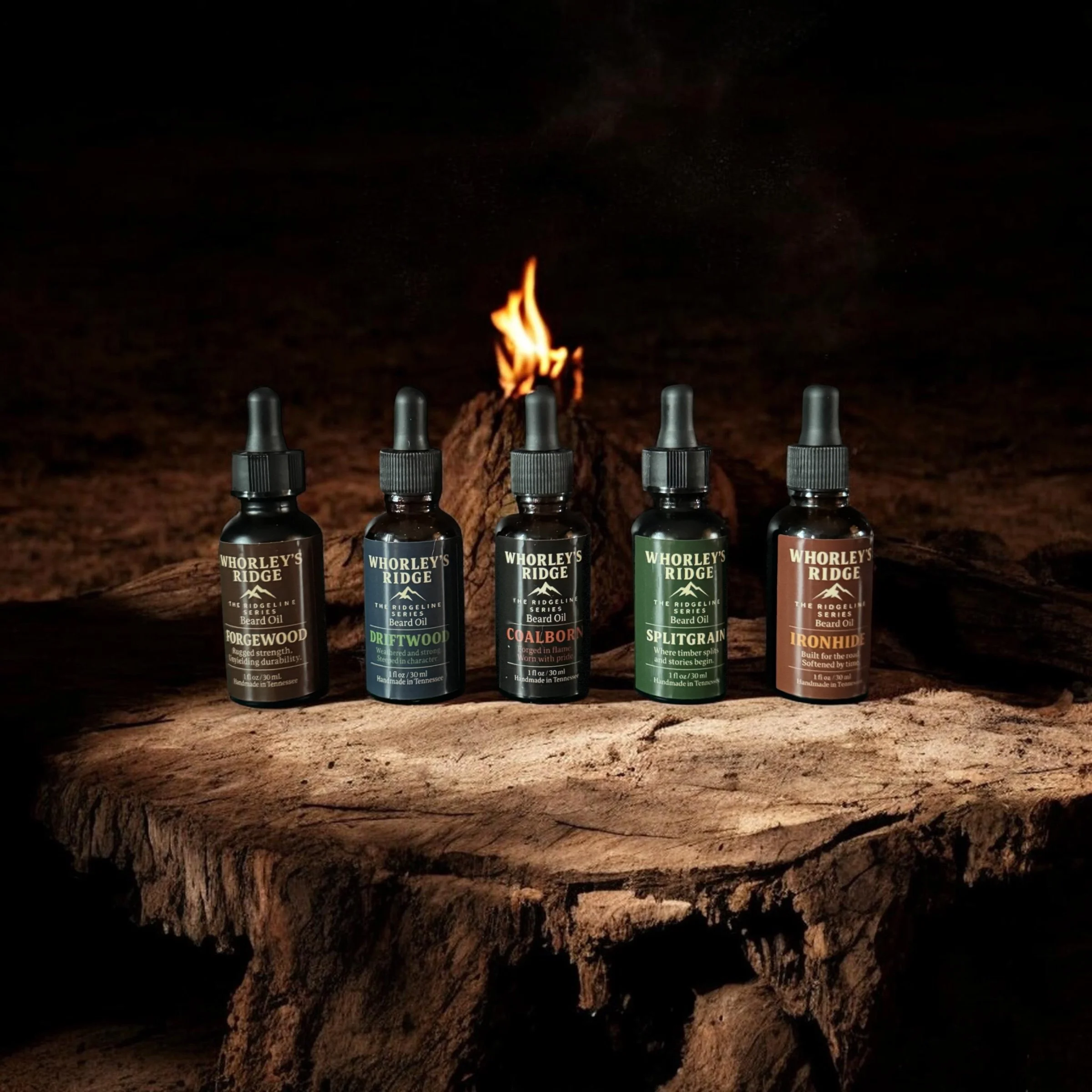 Five bottles of beard oil from Whorley's Ridge arranged on a rough wooden surface with a small fire burning behind them in a dark setting.
