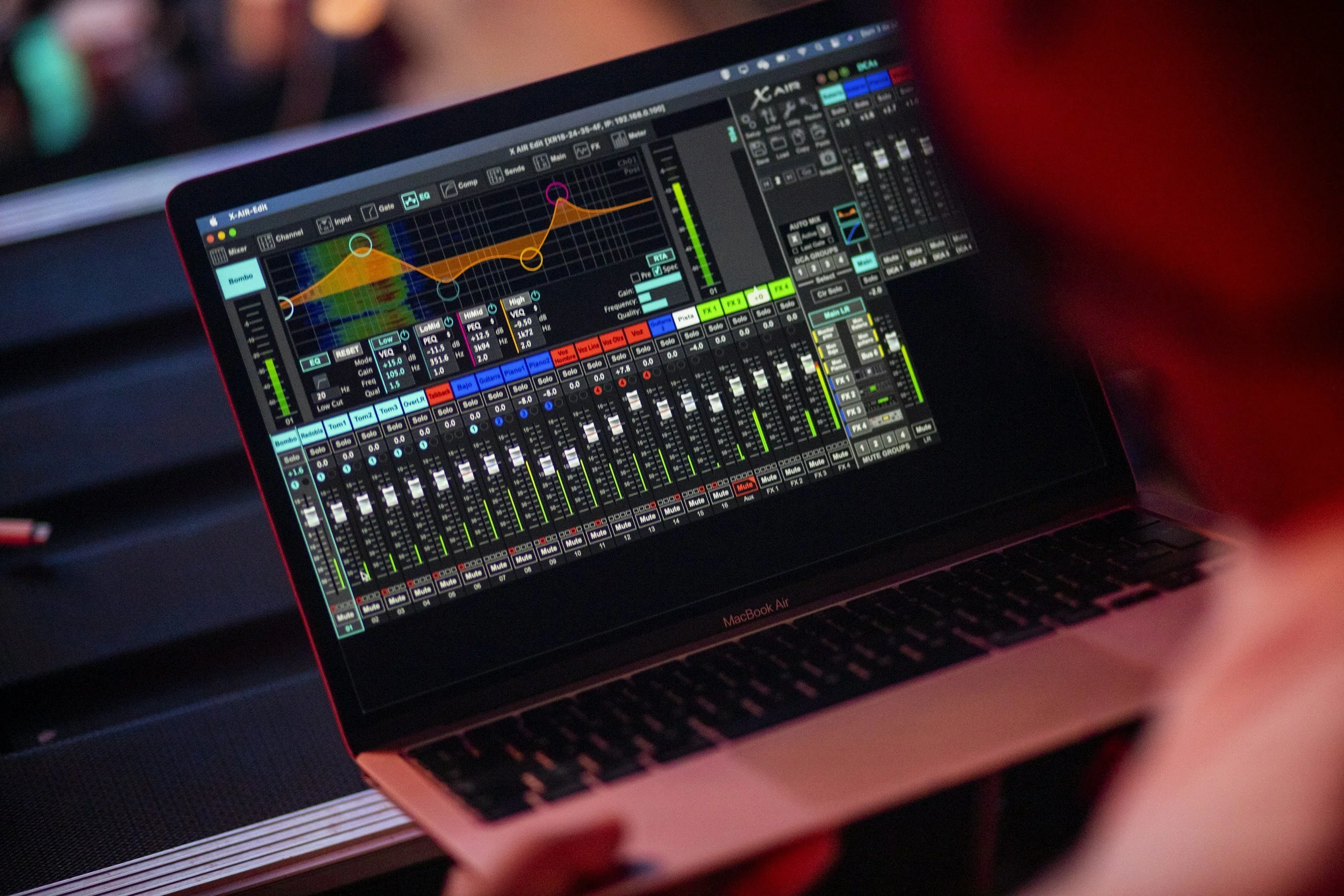 A MacBook Air displaying a digital audio mixing software with multiple sliders, controls, and a colorful audio waveform graph, used for sound editing or DJing.