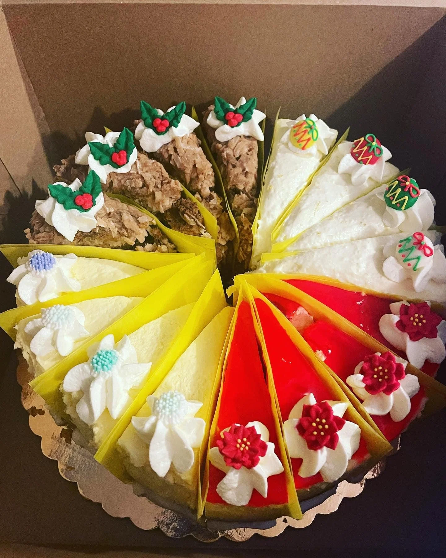 A circular cake decorated with slices of various flavors, each with festive holiday-themed icing and decorations, arranged in a pattern around the cake.