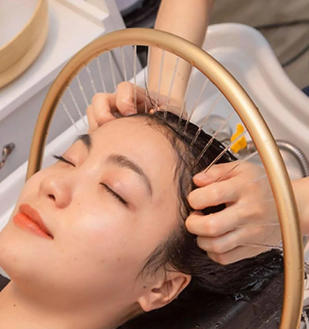 A woman receiving acupuncture treatment on her scalp with thin needles, lying with eyes closed.