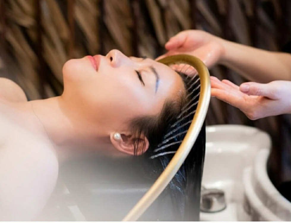 Woman receiving a head massage with water pouring over her hair at a spa.