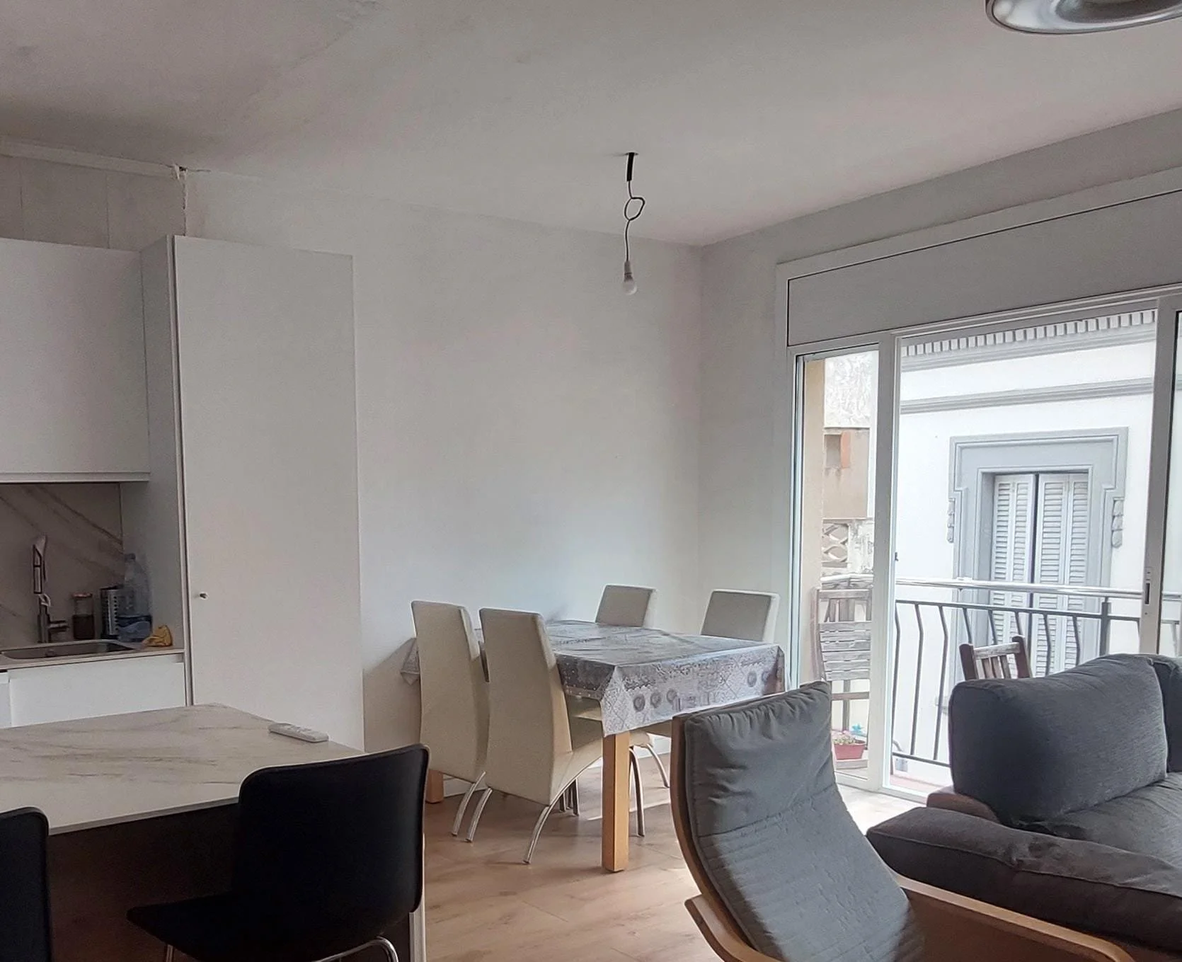 Sala de estar con sillones y comedor, ventana grande con vista a un balcón, luz natural, decoraciones sencillas.