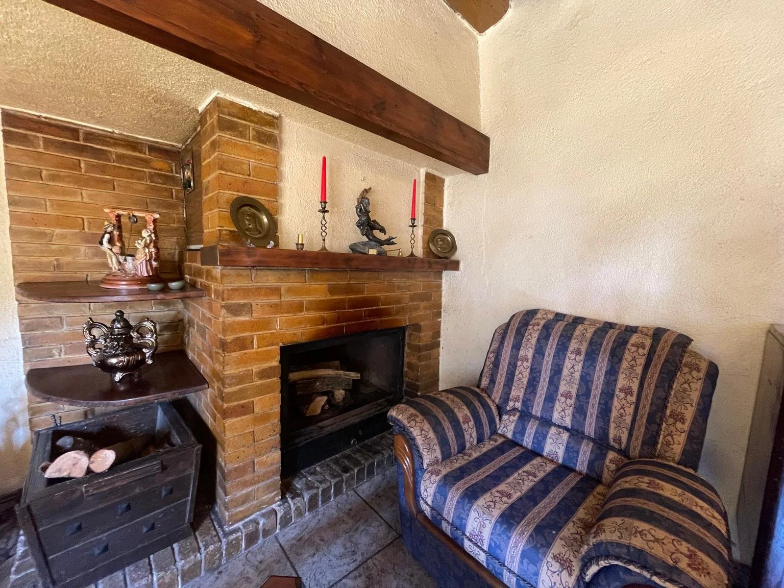 Sala con chimenea de ladrillo, sofá azul con rayas doradas y muebles decorativos en los estantes. Casa en Malgrat de mar.