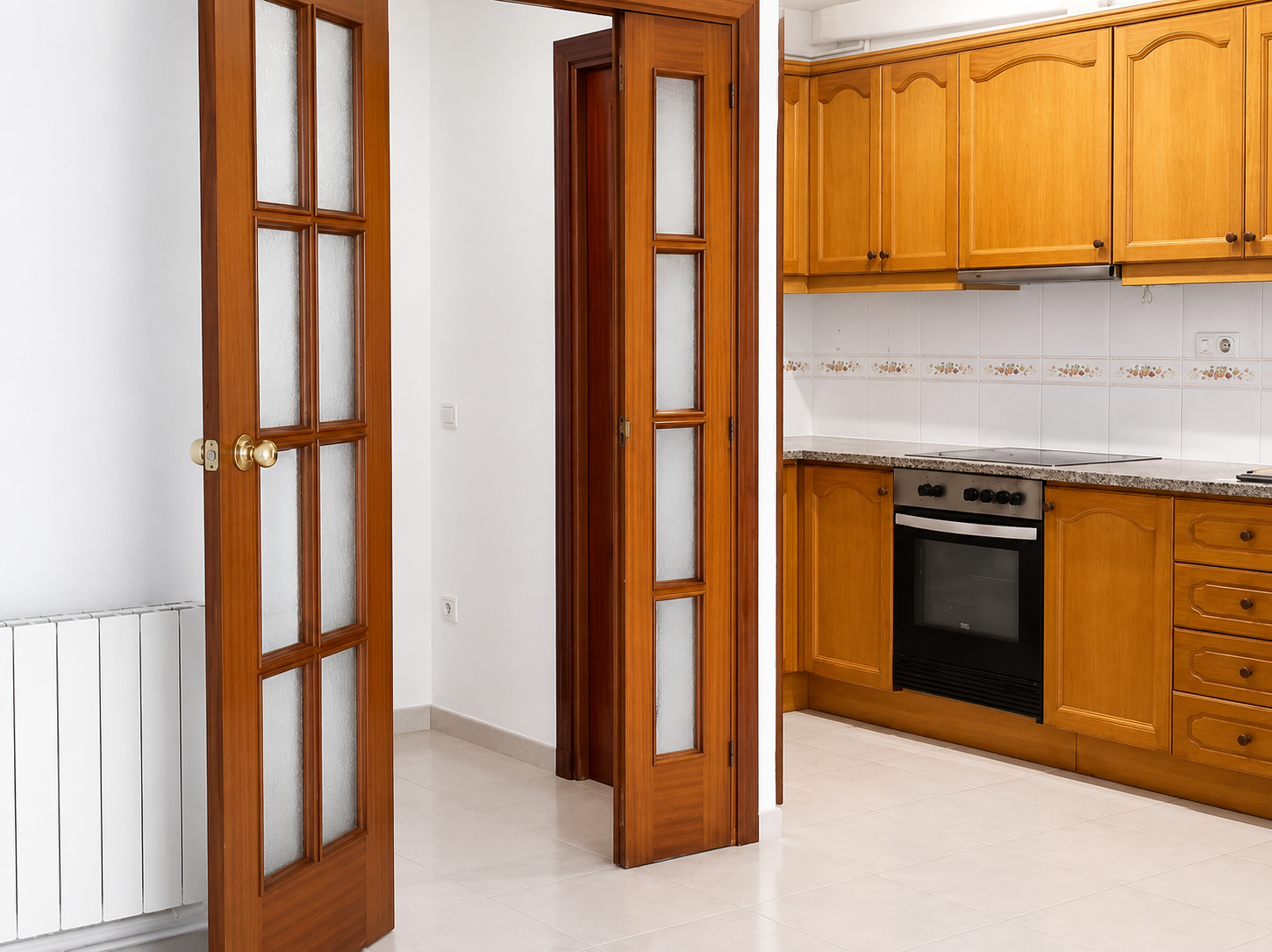 Cocina con gabinetes de madera, horno eléctrico, encimera de granito, paredes decoradas con azulejos con diseño floral, puertas de madera con paneles de vidrio
