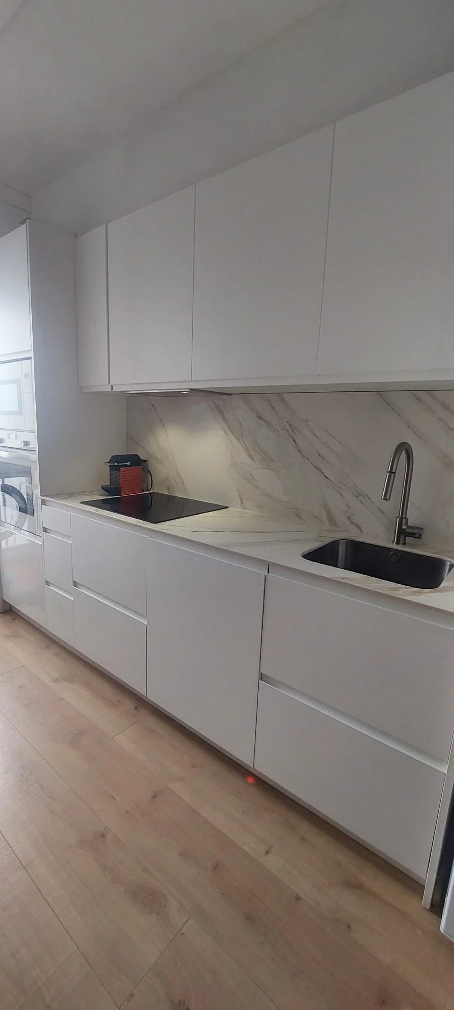 Cocina moderna con encimera de mármol, fregadero y armarios blancos.
