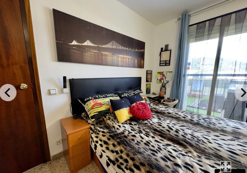 Habitación con una cama de dosel con ropa de cama con patrón de leopardo, varias almohadas y cojines decorativos, un cuadro grande de un puente en la pared, una ventana con cortinas azules y una terraza con vista al exterior.