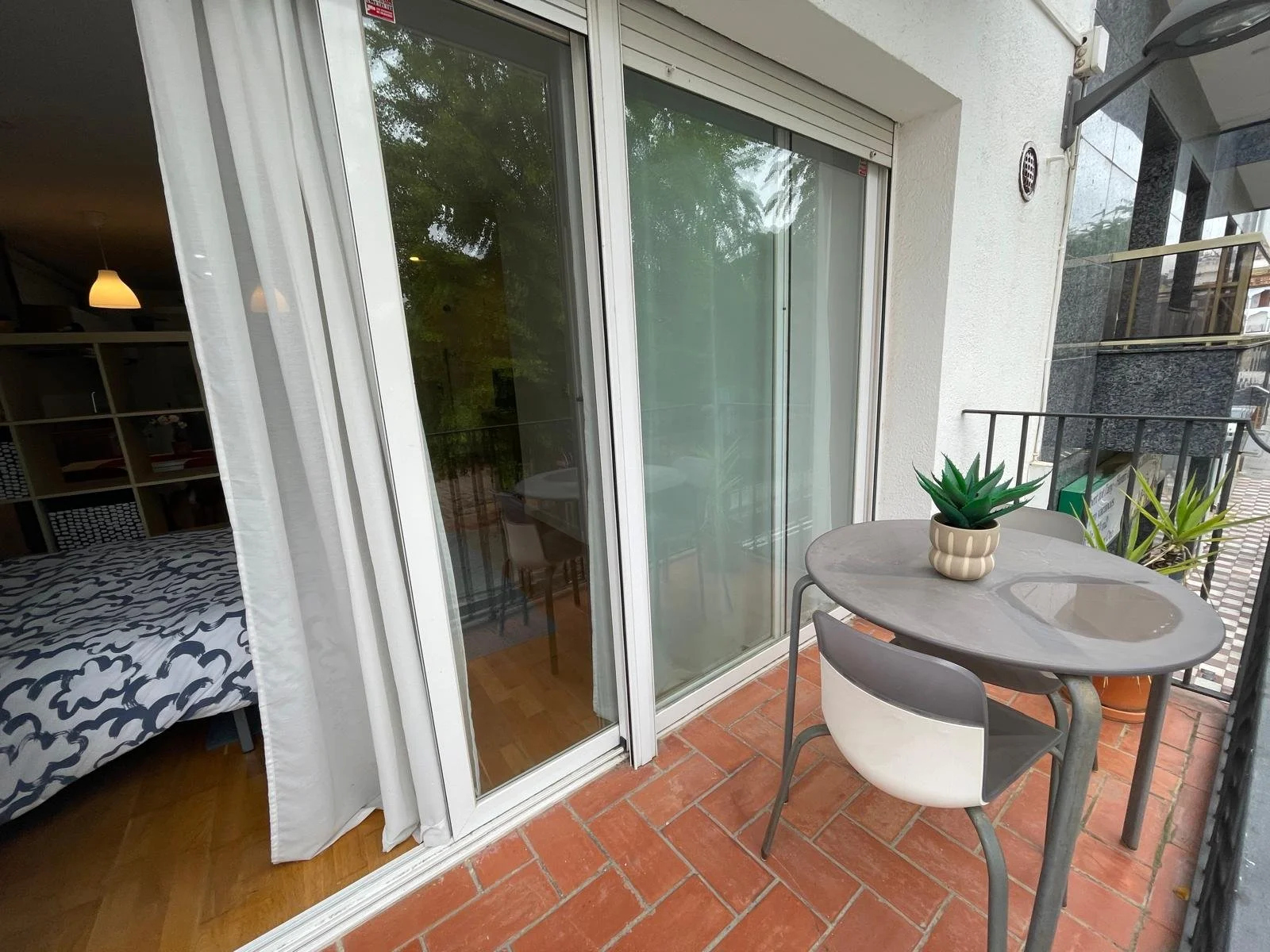 Balcony with a small round table and two chairs, decor with two potted succulent plants, and glass sliding door leading to the interior of an apartment.