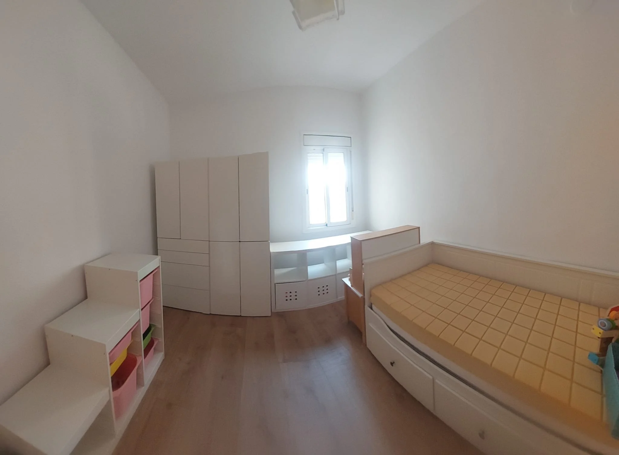 Habitación infantil con cama, mueble de guardado, estantería y ventana, decorada en colores suaves.