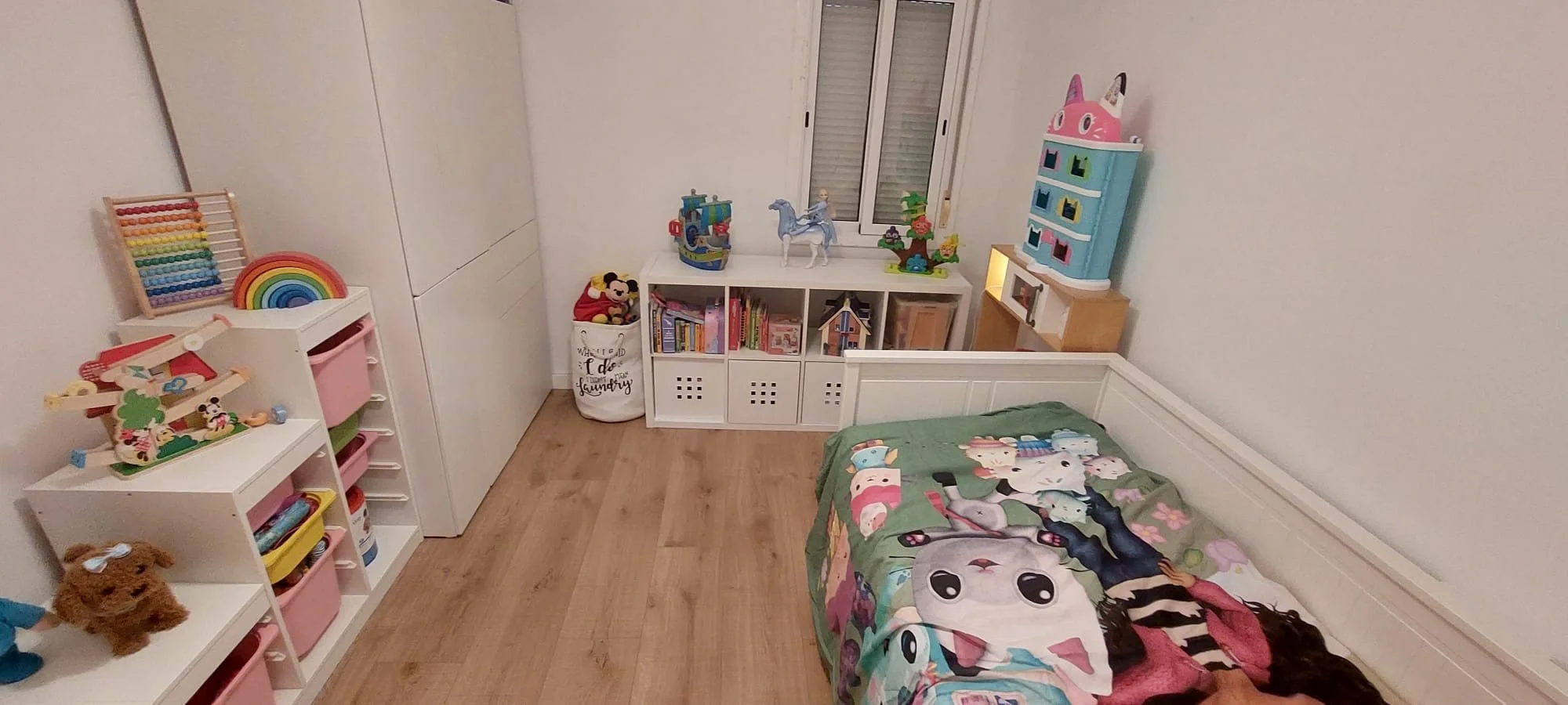 Dormitorio infantil con cama, estanterías llenas de juguetes y libros, decoraciones coloridas y una ventana.