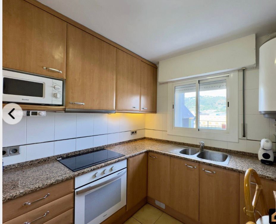 Cocina con gabinetes de madera, encimera de granito, horno, estufa eléctrica, microondas, fregadero doble y vista a un paisaje Montañoso a través de la ventana.