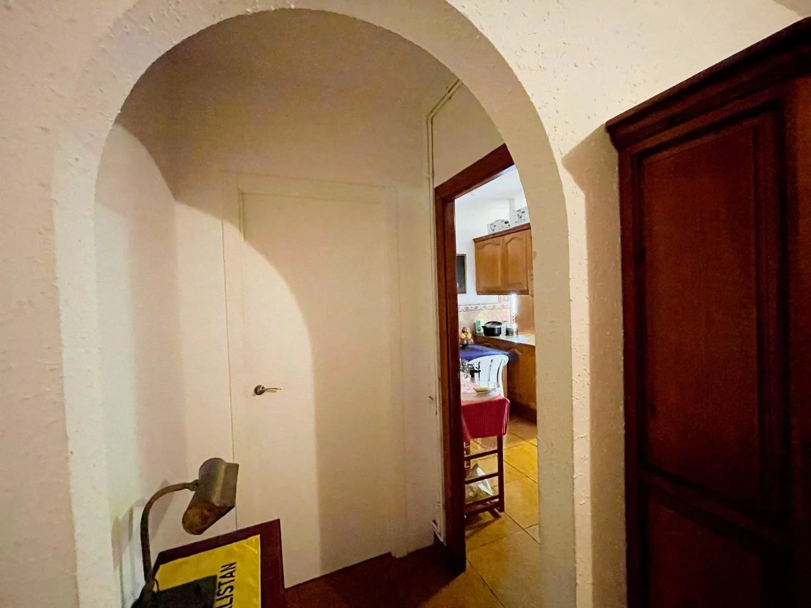 Vista de un pasillo que conduce a una cocina, con un armazón de madera y un armario grande de madera a la derecha, en una vivienda con paredes texturizadas y puerta blanca en el fondo.