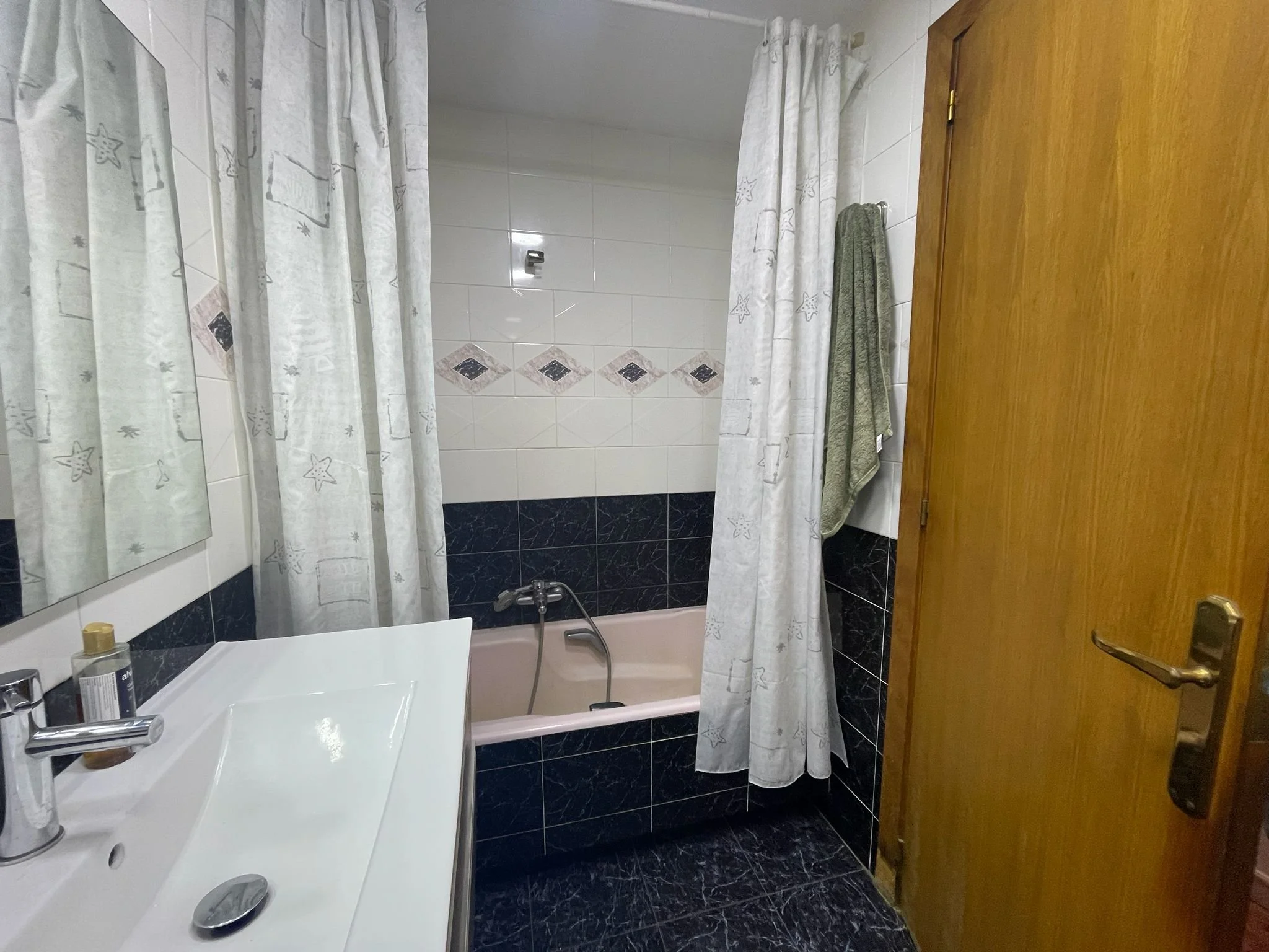 Baño con ducha, cortinas con estrellas, lavabo, espejo, toalla en la pared y puerta de madera.
