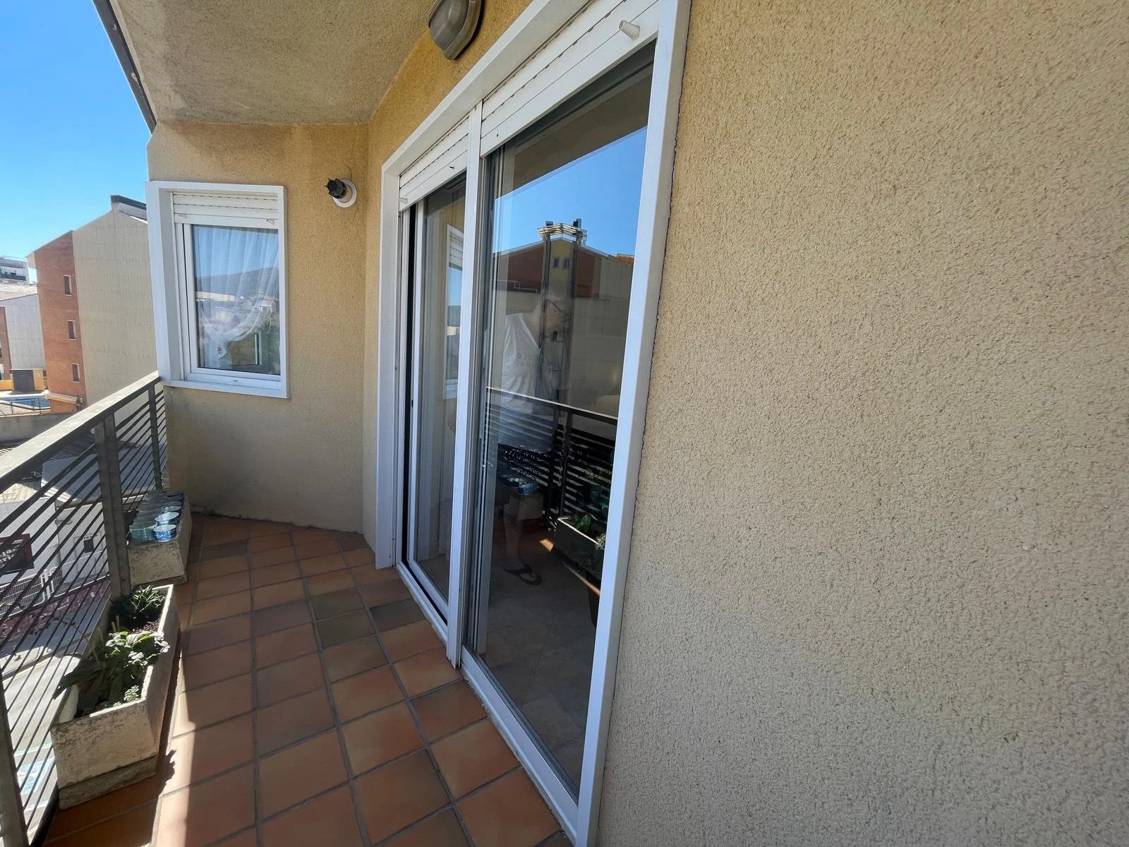 Balcón de un apartamento con puertas de cristal corredizas y una ventana, plantas y algunos objetos decorativos