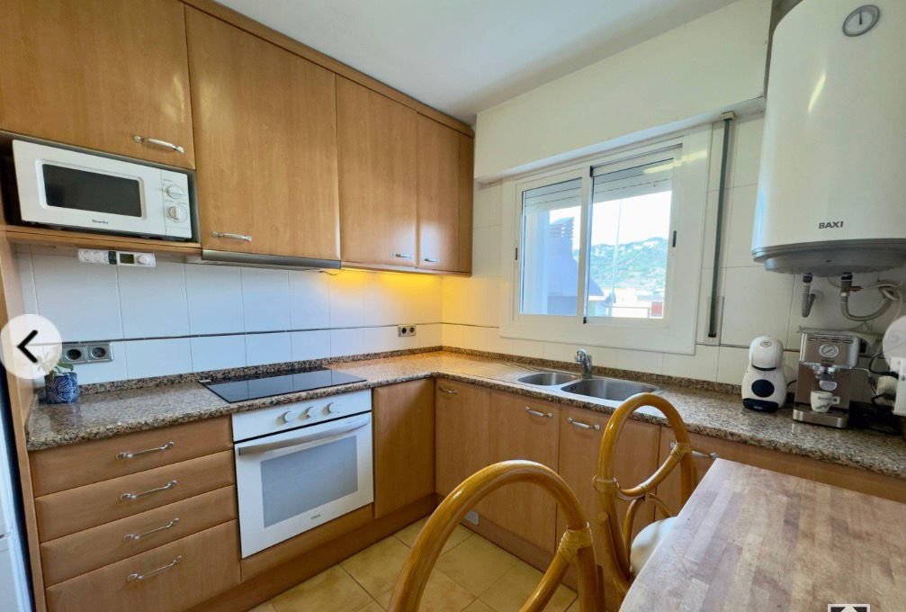 Cocina con gabinetes de madera, encimera de granito, horno, microondas, fregadero doble, ventana grande, y electrodomésticos blancos.