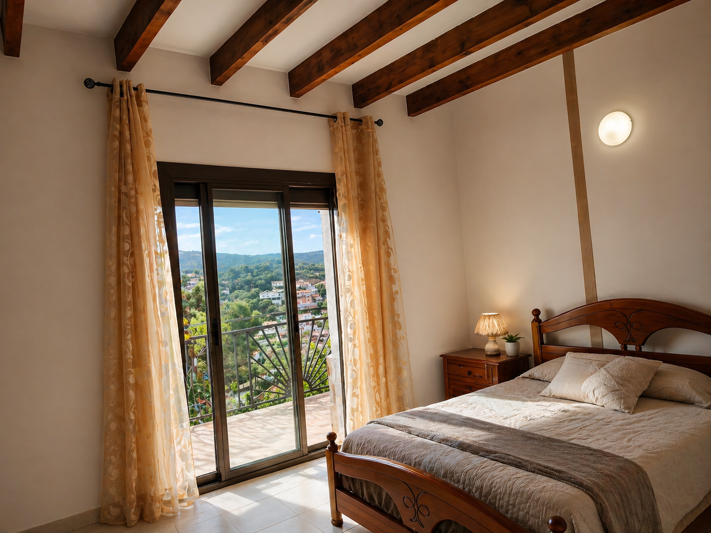 Habitación con puerta de balcón que da a una vista de colinas verdes y casas, cortinas beige, cama de madera con ropa de cama clara y lámpara de noche con lámpara de mesa y planta.