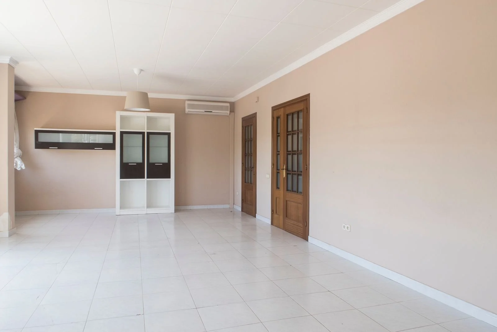 Sala vacía con paredes beige, puertas de madera con cristaleras, aire acondicionado y armario con puertas de cristal