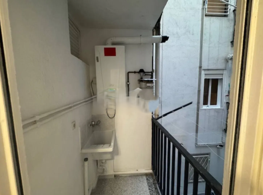 Vista de un balcón con una lavadora automática, un lavadero y tuberías en una pared