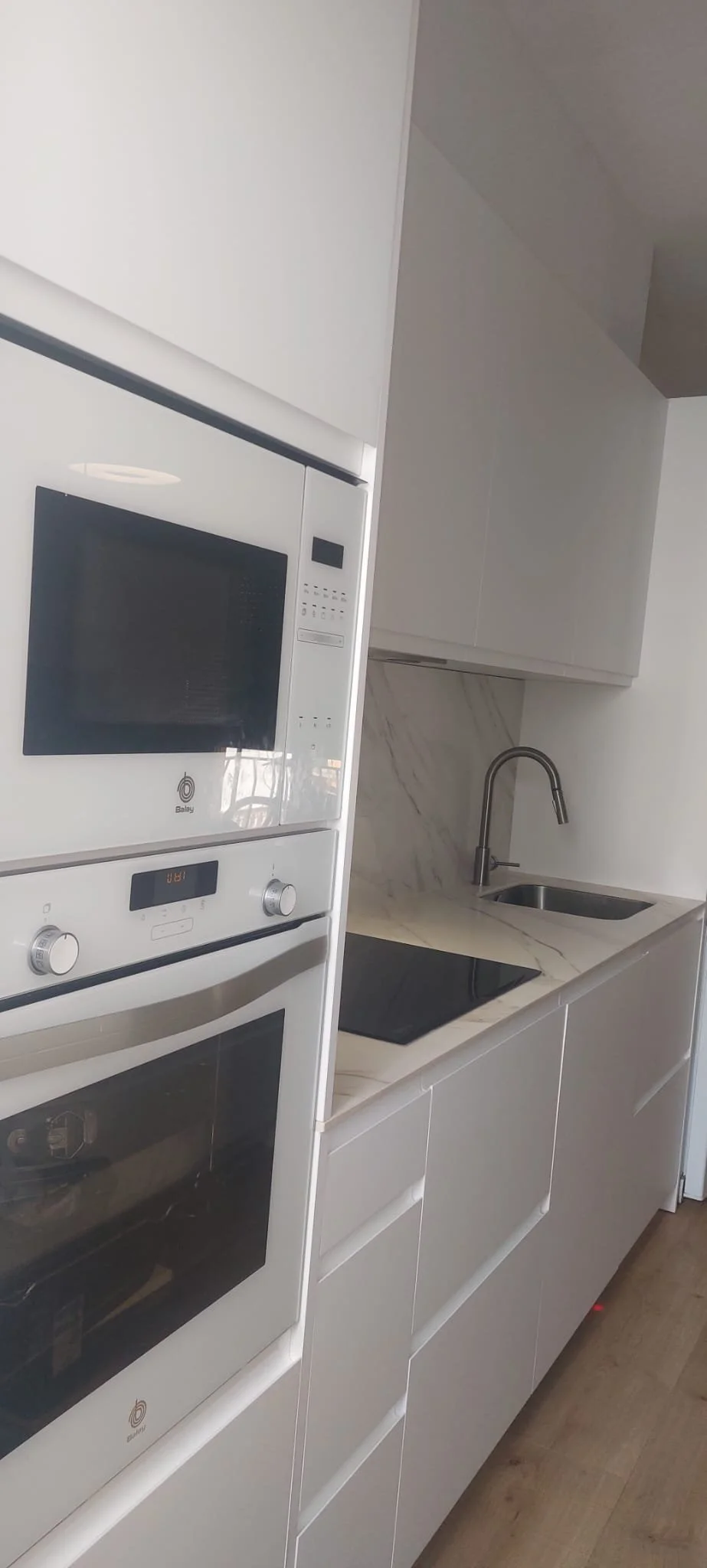 Cocina moderna con horno, microondas, fregadero y encimera de piedra.