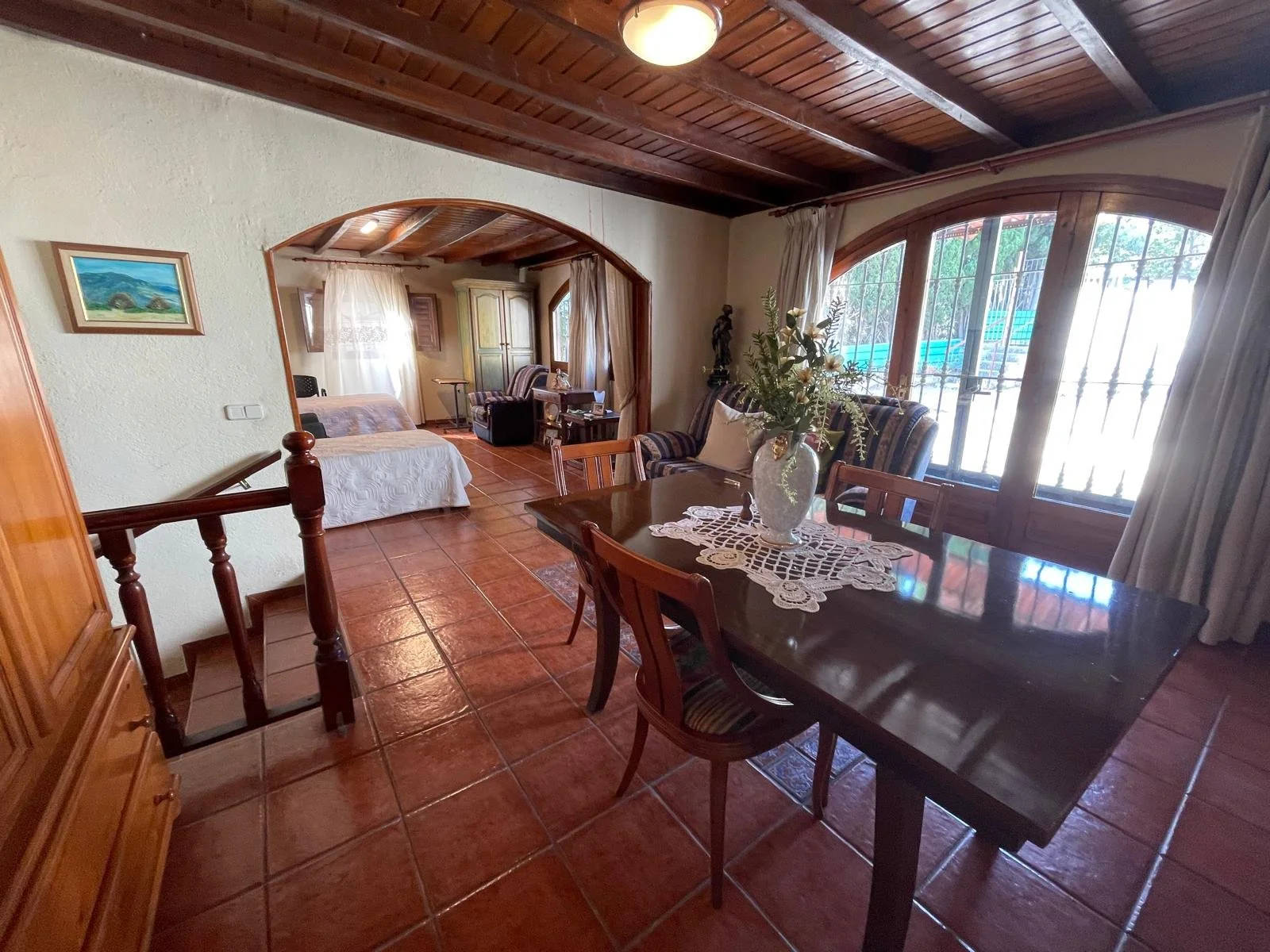 Sala de estar y comedor con piso de cerámica, muebles de madera, ventanas grandes con cortinas, y una decoración clásica con flores. Casa en Malgrat de mar.