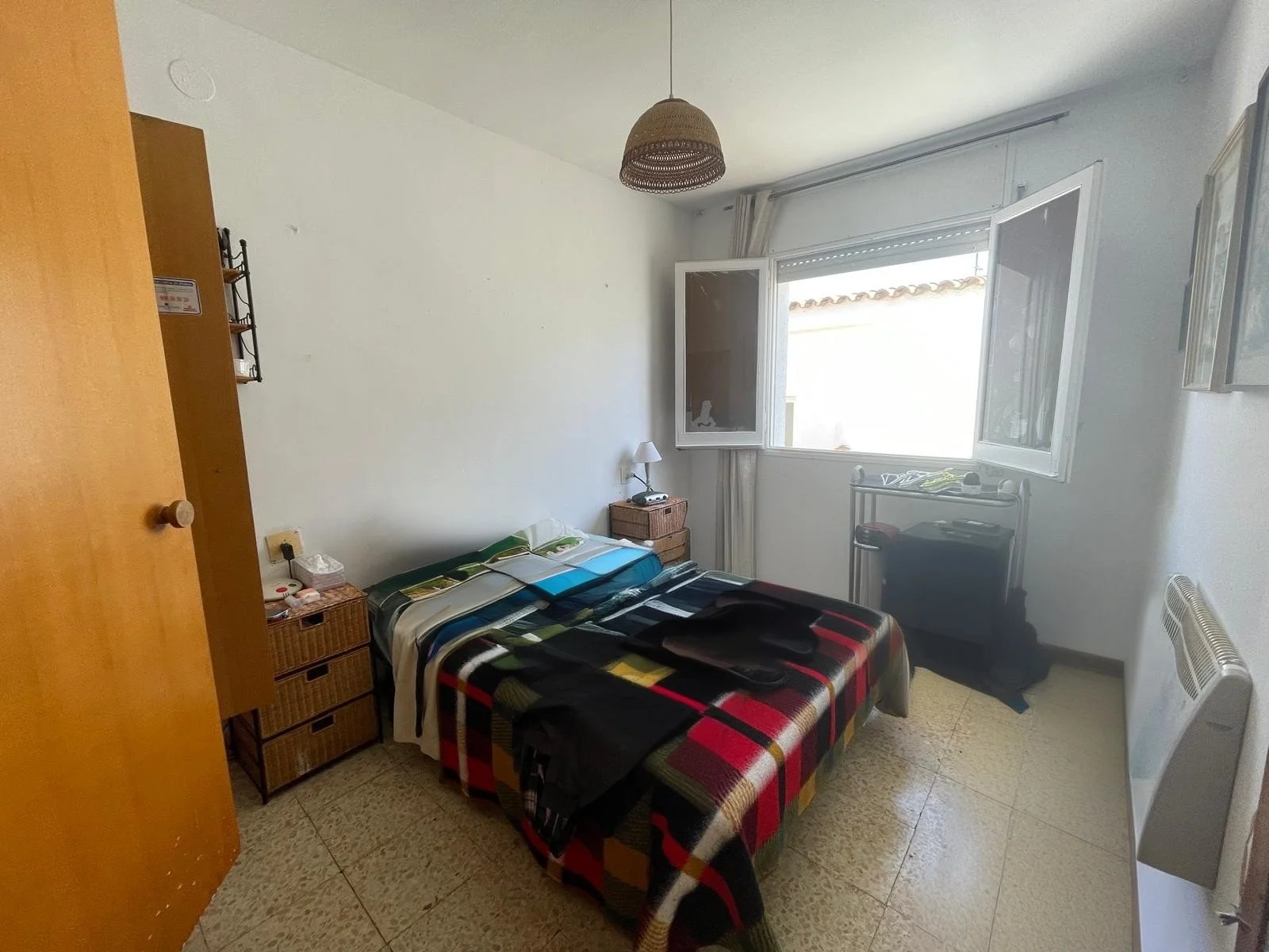Habitación sencilla con cama, mesitas de noche y ventana abierta.