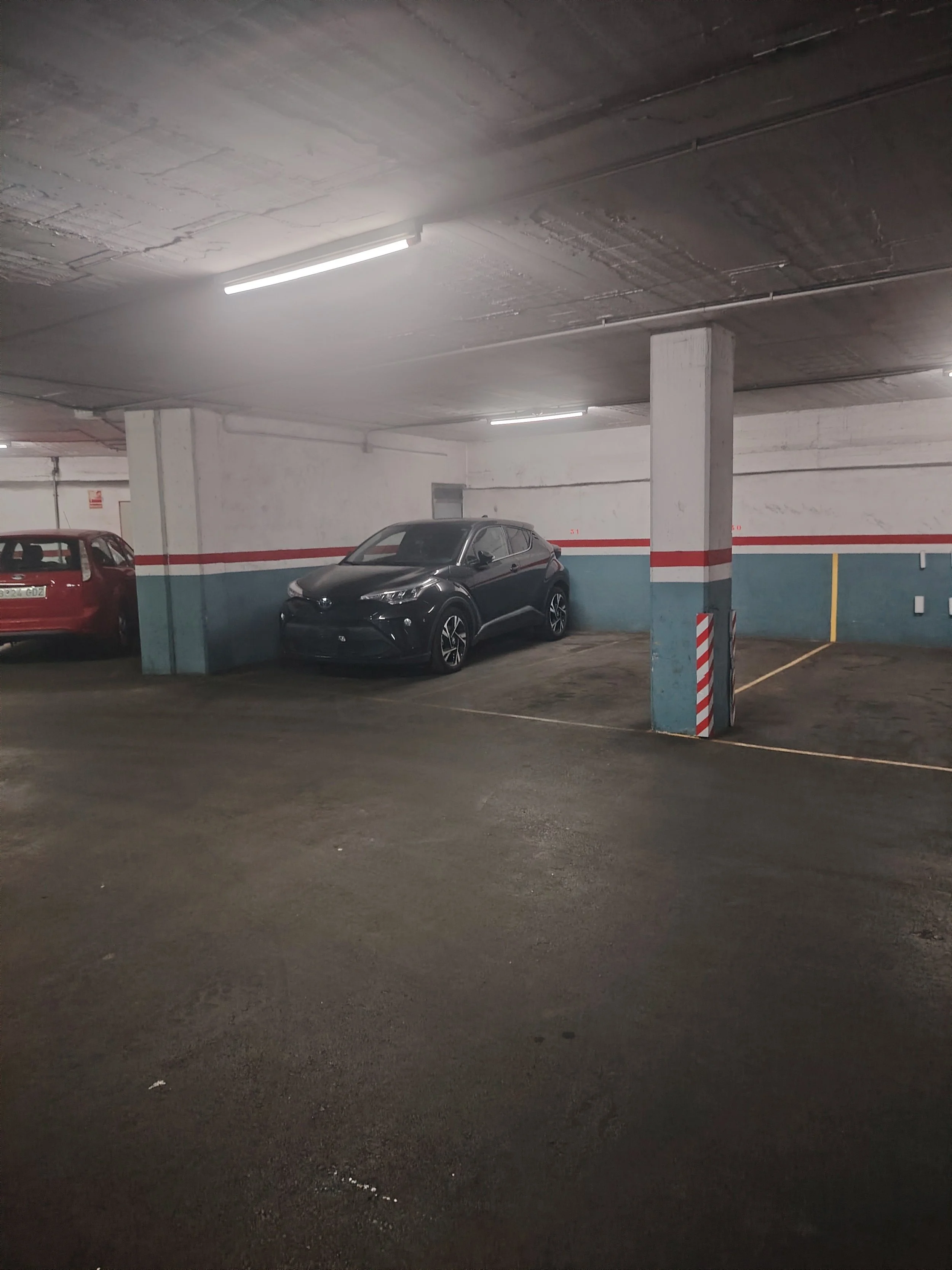 Estacionamiento subterráneo con dos autos y columnas con pintura a rayas blancas y rojas.