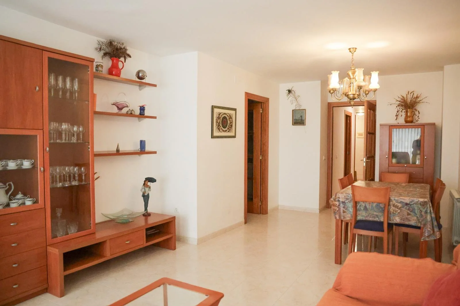 Sala de estar con armario de madera, estanterías con objetos decorativos, mesa con sillas, candelabro en el techo y decoración en las paredes.