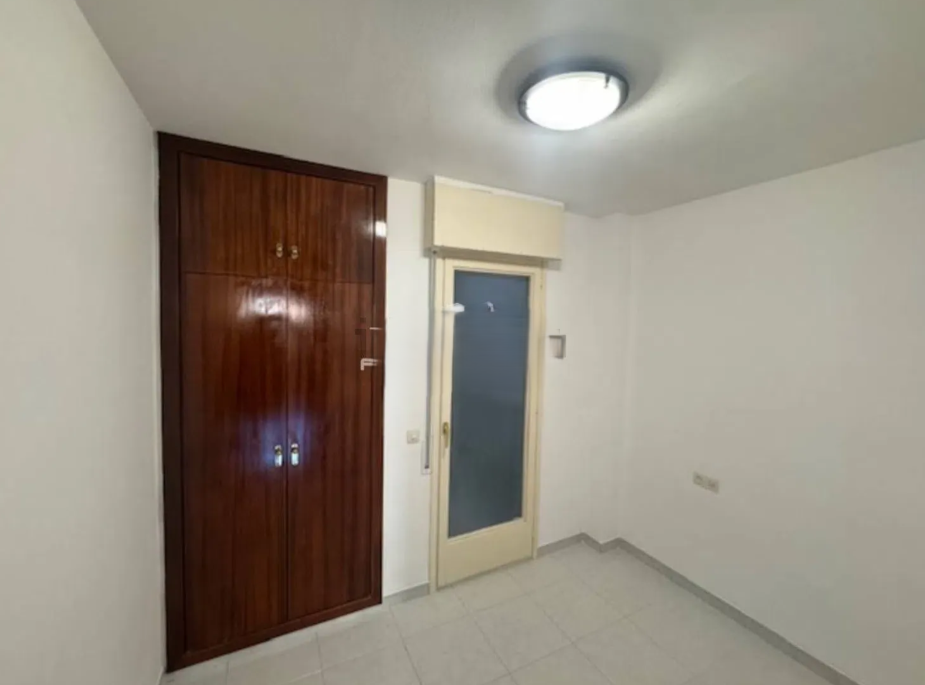Habitación con pared blanca, armario de madera, puerta de vidrio y luz de techo