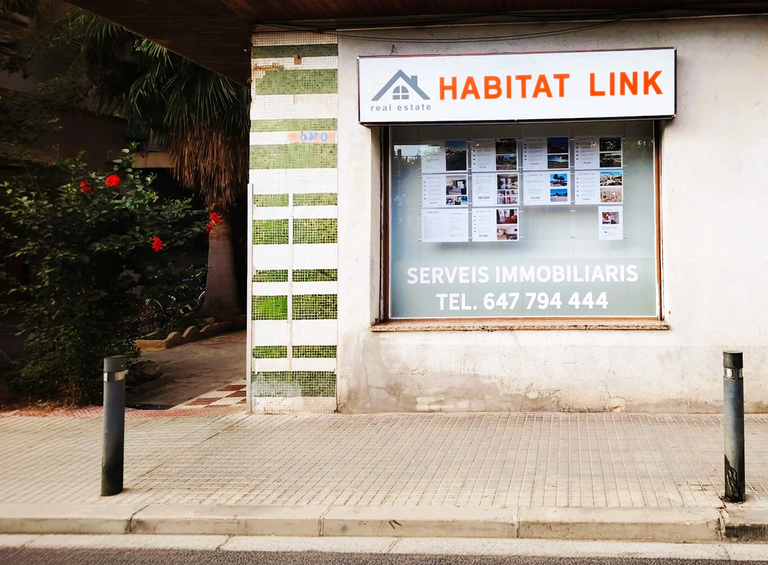 Cartel de agencia inmobiliaria llamado 'Habitat Link' con información de contacto y anuncios en la ventana.