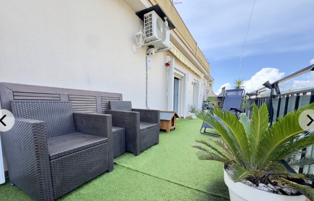 Terraza con sillas de mimbre, plantas y vista al cielo y edificios.