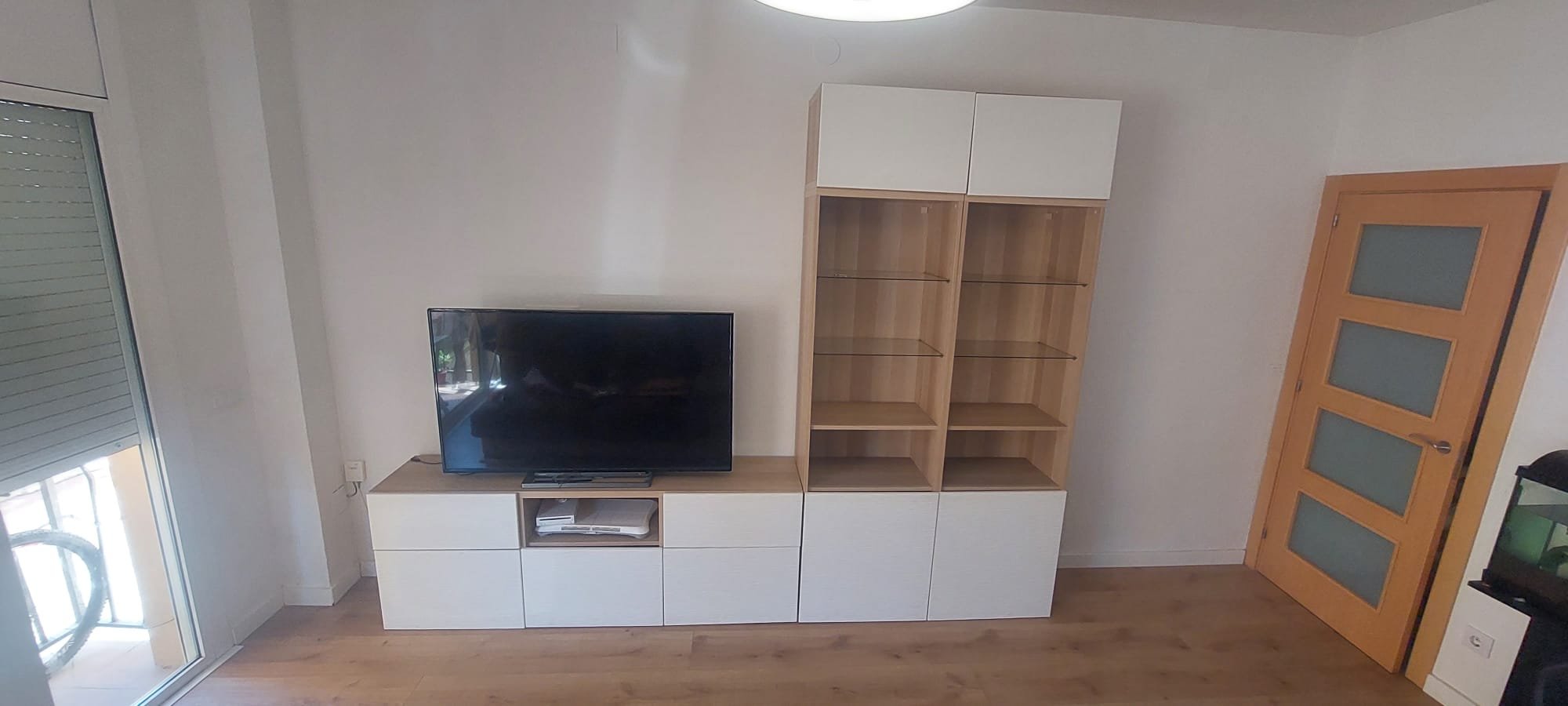 Sala de estar con televisión en mueble bajo, librero de madera y puerta de madera con ventanas de vidrio opaco.