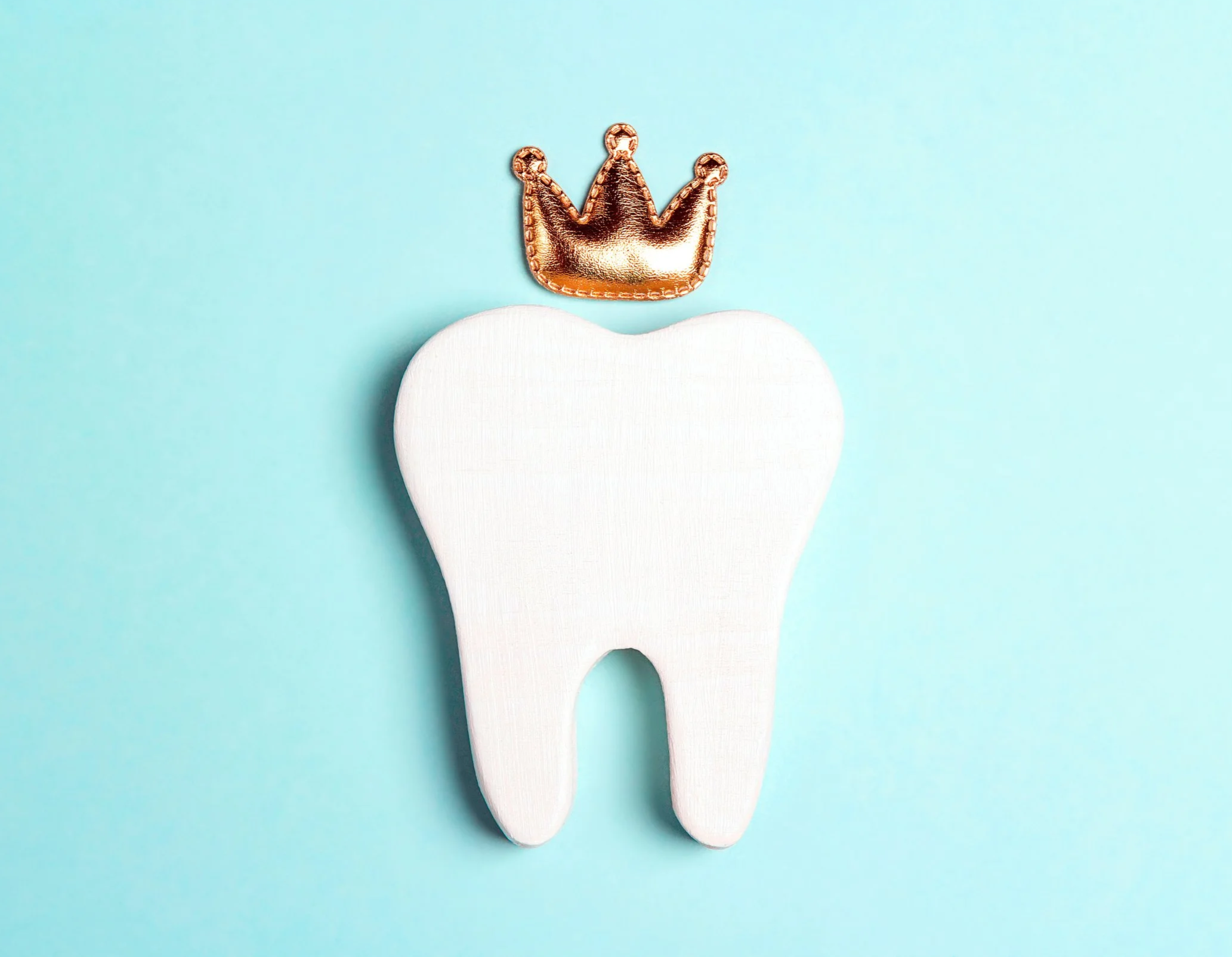 A white tooth-shaped object with a small metallic gold crown above it, placed on a light blue background.