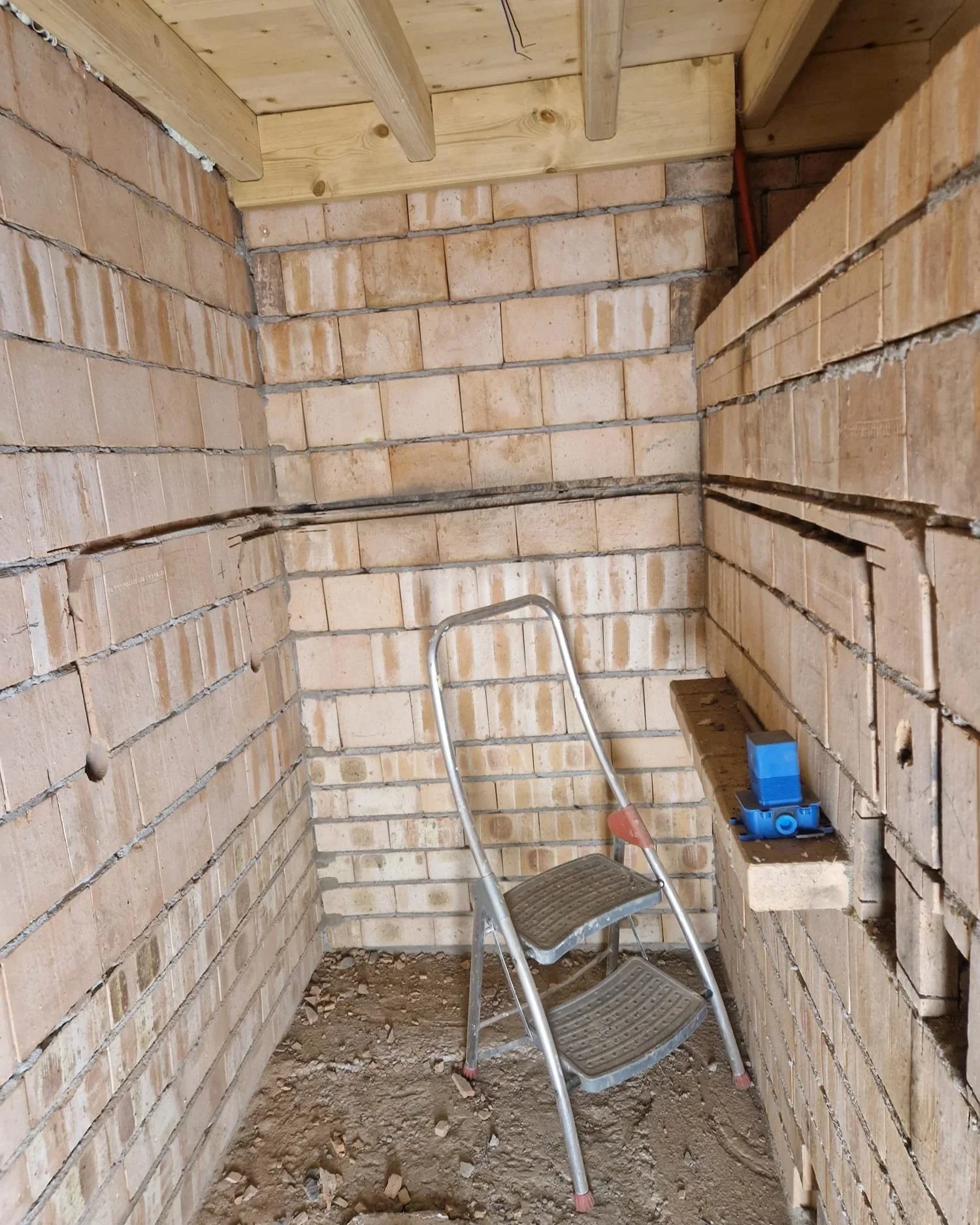 Binnenruimte van een bouwconstructie met bakstenen muren, een trap en bouwmaterialen, klaar voor verdere afwerking.