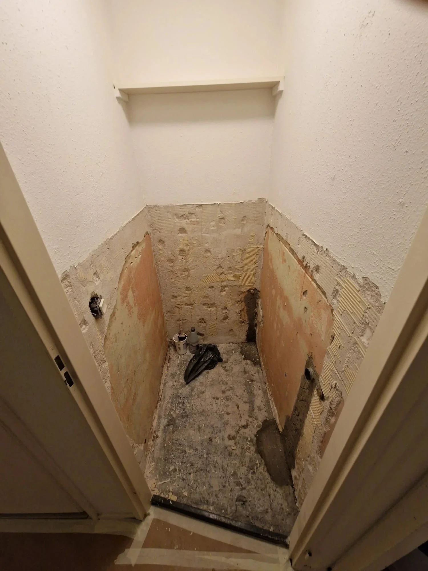 Een kleine kamer onder renovatie, met blootgelegde muren en vloer, bouwmaterialen en gereedschap in de kamer.