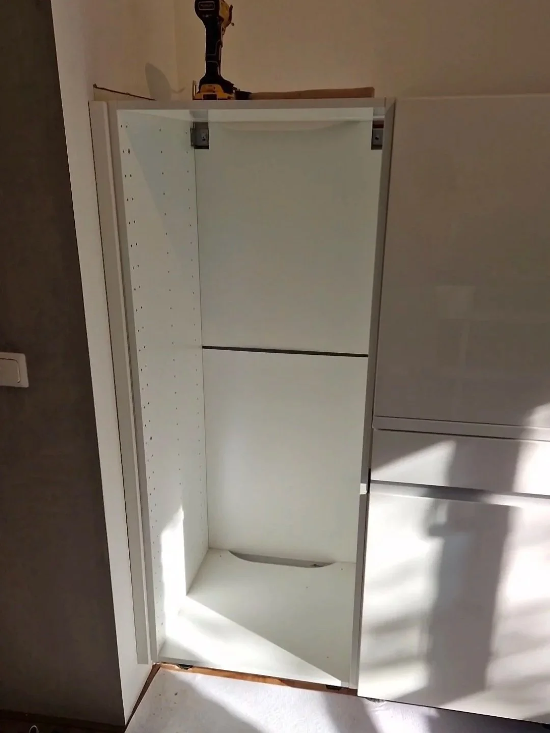 Onbehandeld witte kast zonder deuren, geplaatst voor een muur, met een scharnier en een boor op de bovenkant.