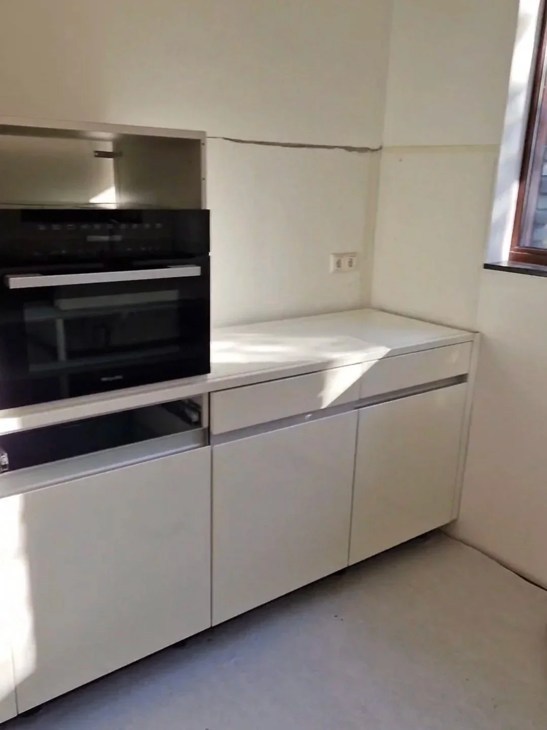 Leeg keukenkastje met een ingebouwde oven en een stopcontact op de muur