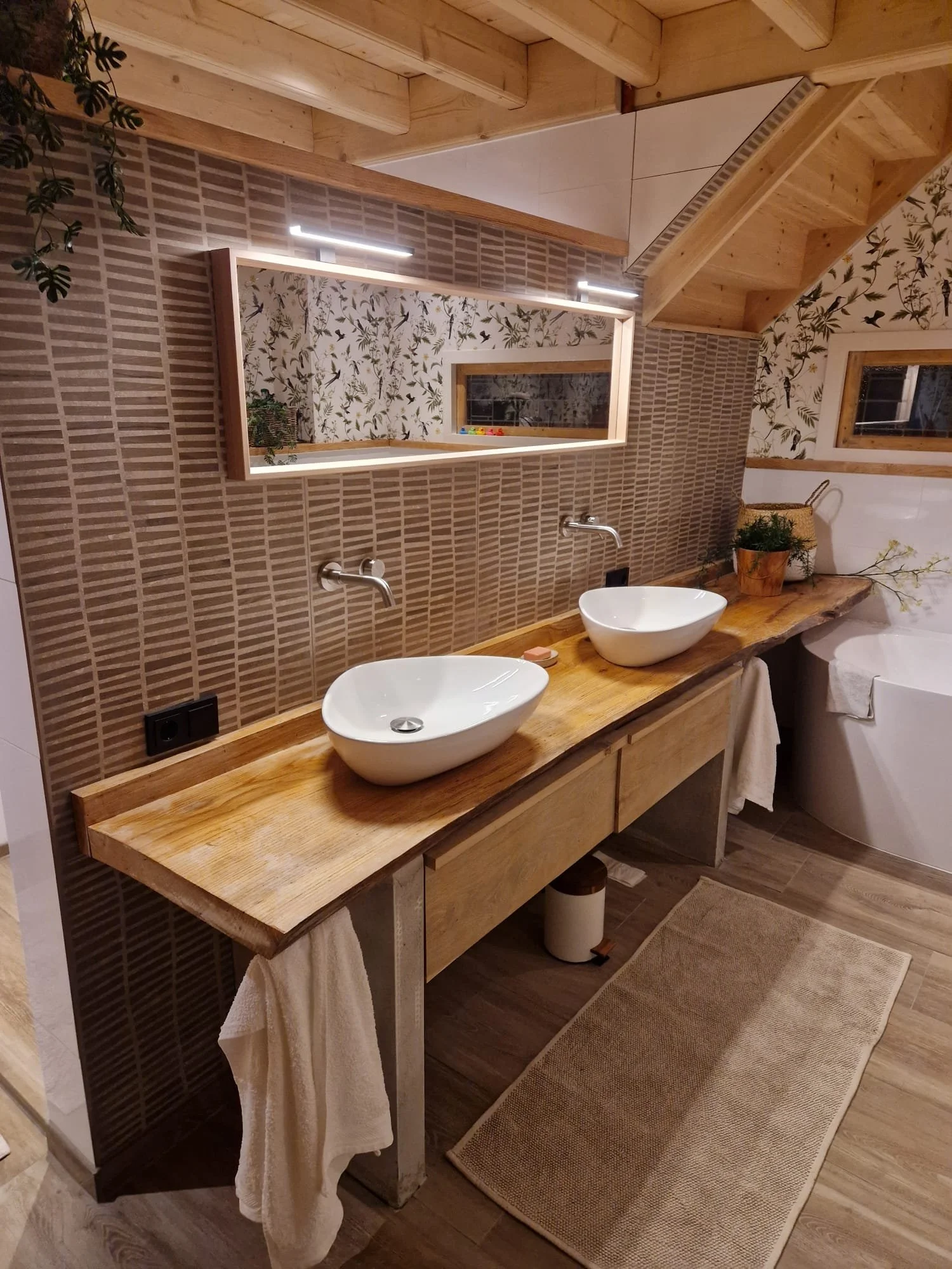 Een badkamer met twee wazige wasbakken op een houten aanrecht, een grote spiegel, planten, en een houten plafond en vloer.