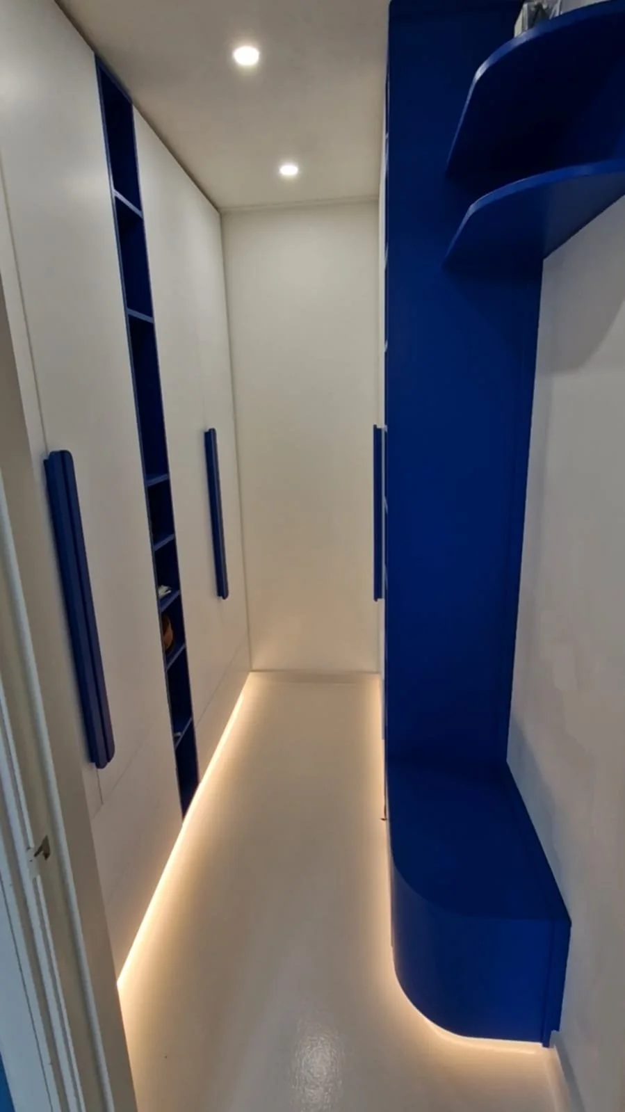 A modern walk-in closet with white and blue cabinets, built-in shelves, and LED lighting along the floor.