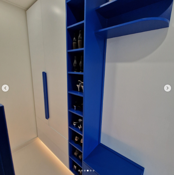 Blue shoe storage shelves with a few pairs of shoes, adjacent to white cabinets with long blue handles, in a closet or hallway.